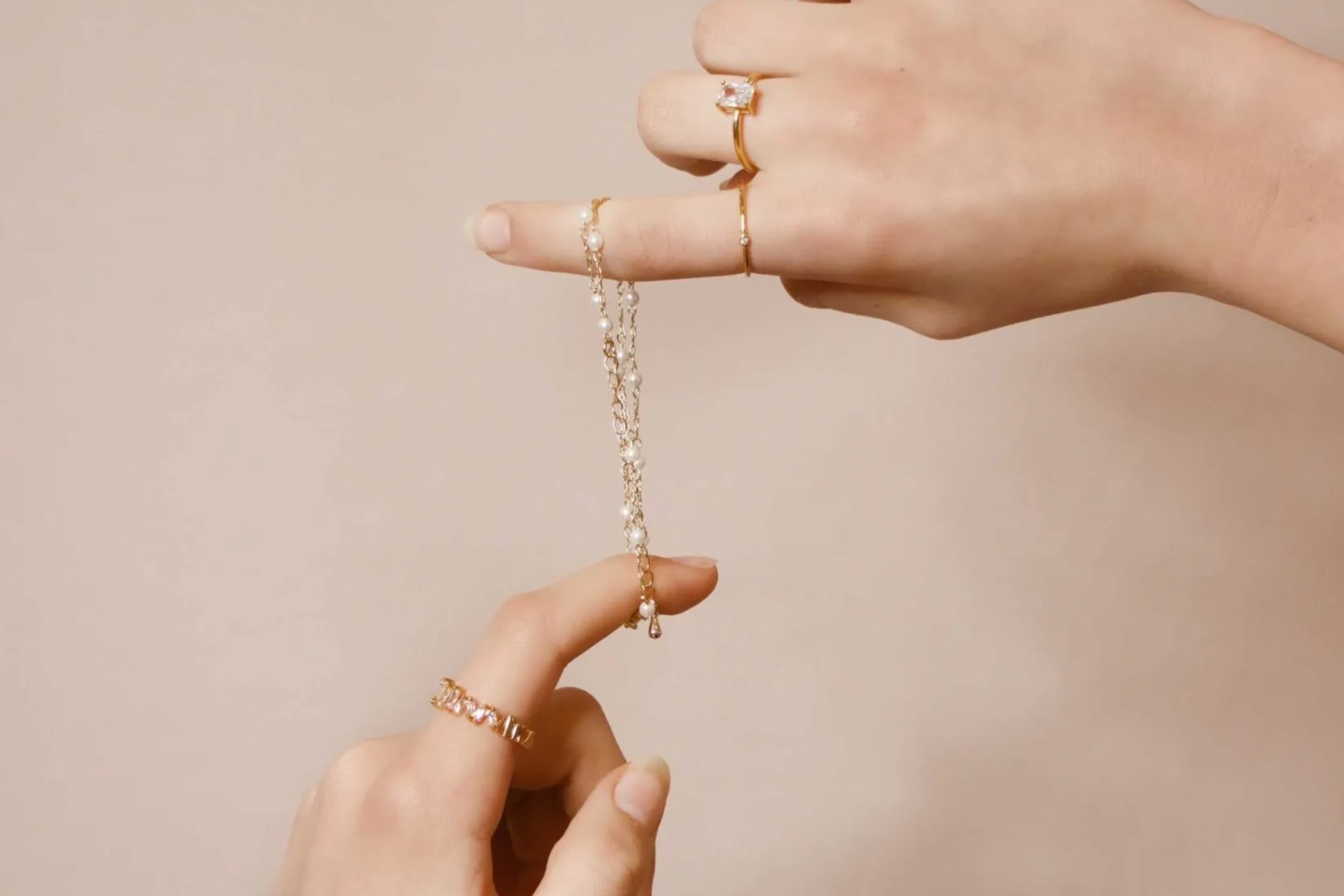 A woman's hand holding a dainty bracelet with pointing fingers
