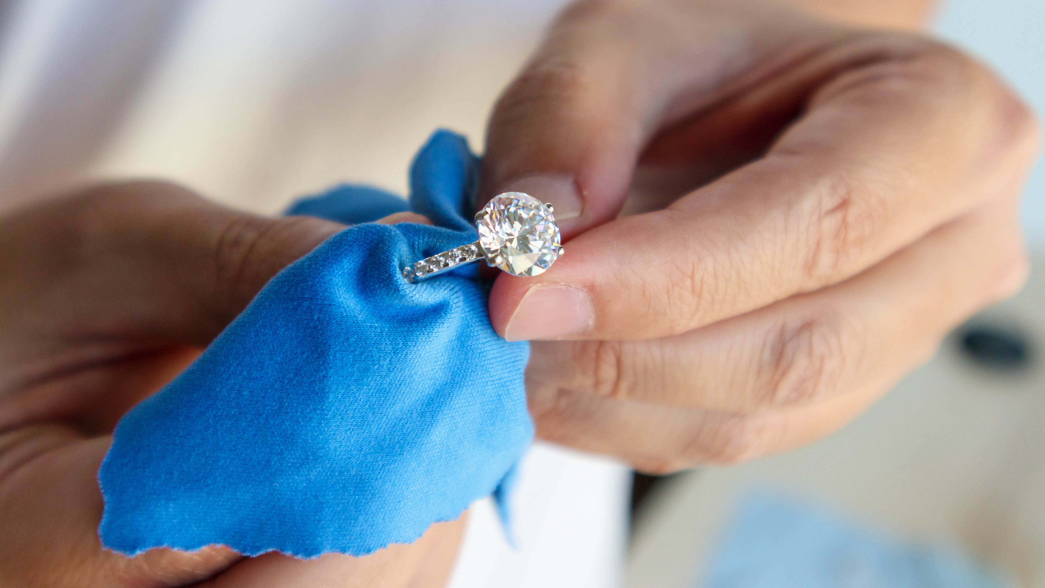 A person cleaning a round cut diamond ring with soft blue cotton