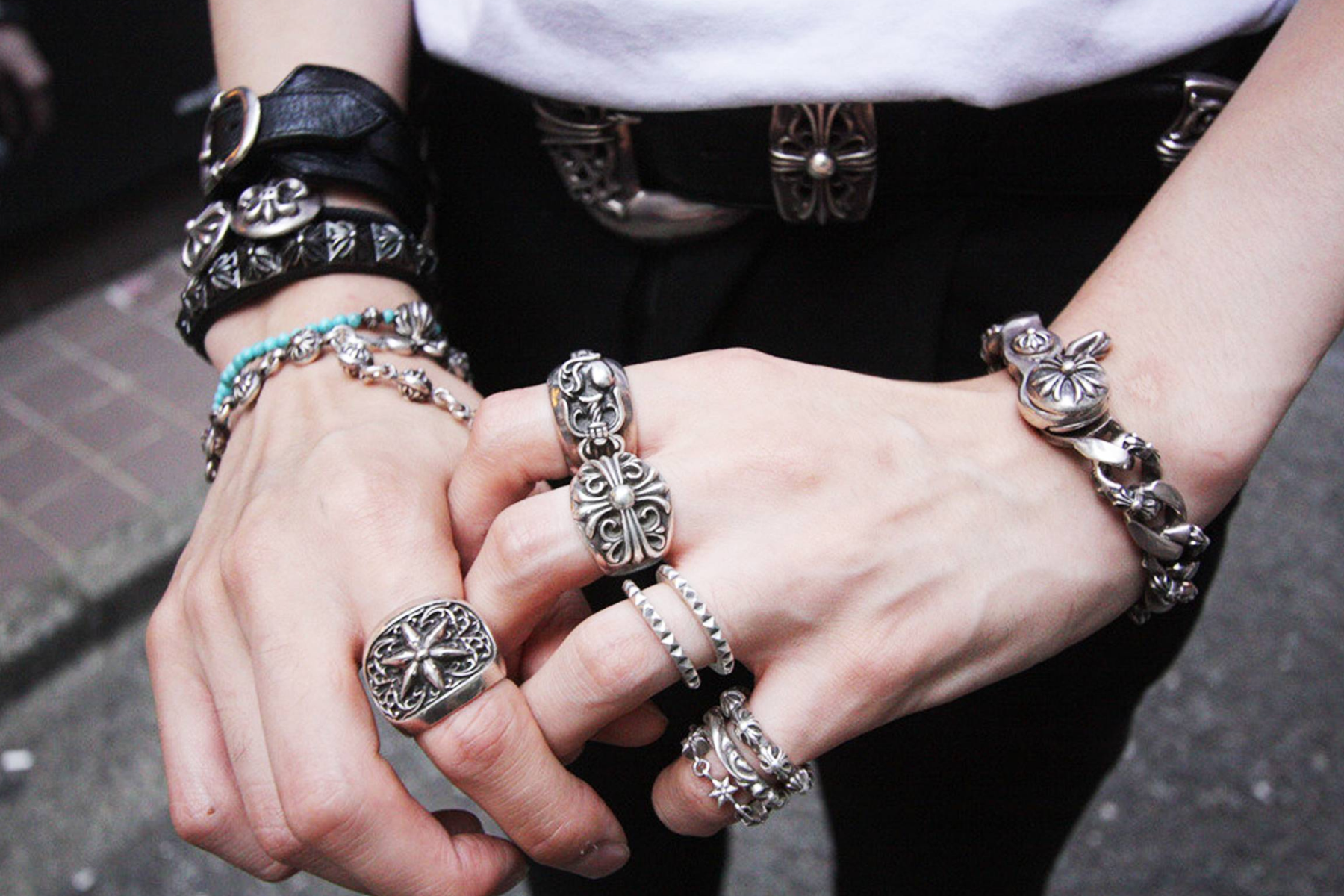 A man's hand adorned with various pieces of silver jewelry