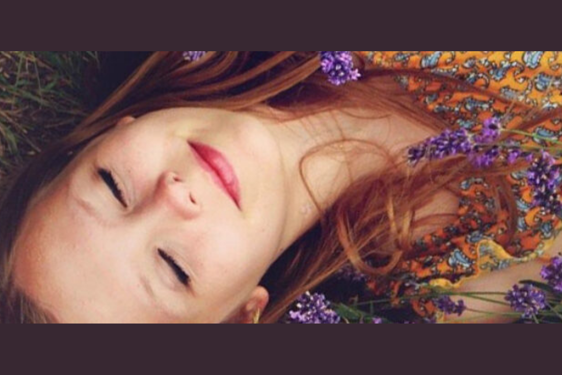 A young girl lies down on the grass, violet flowers on her chest
