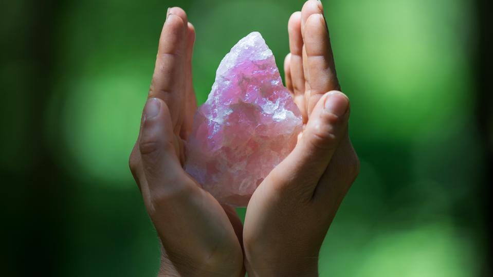 A close-up view of a woman's hand holding a small, pink chakra stone