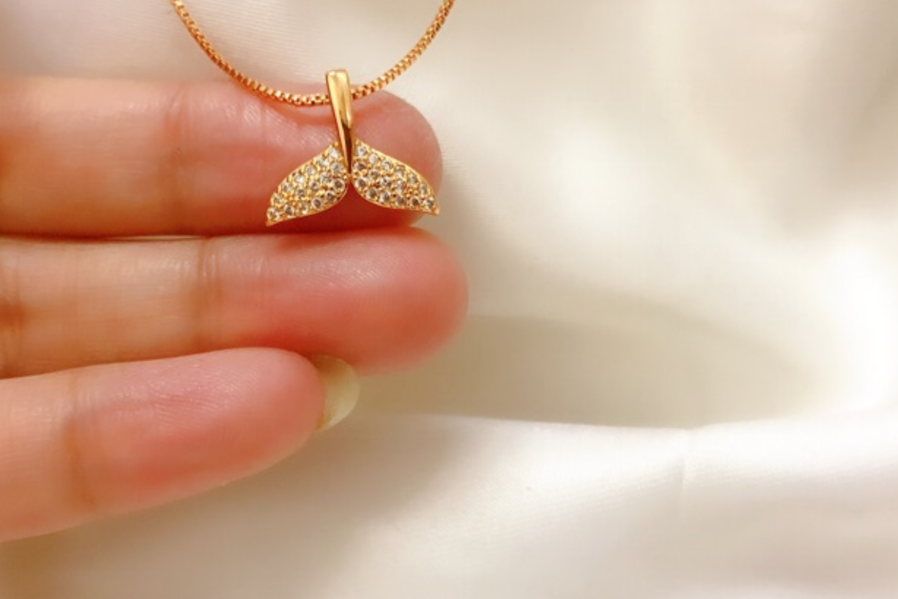 A woman's hand holding a gold mermaid pendant necklace