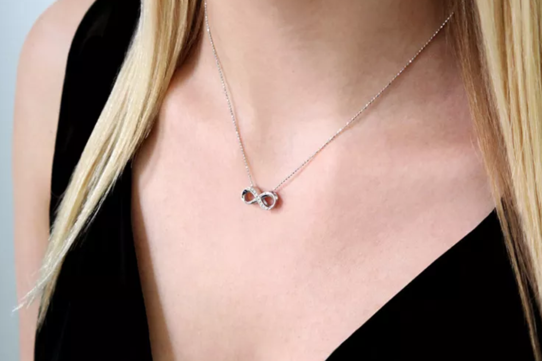 A silver infinity necklace is worn by a blonde woman