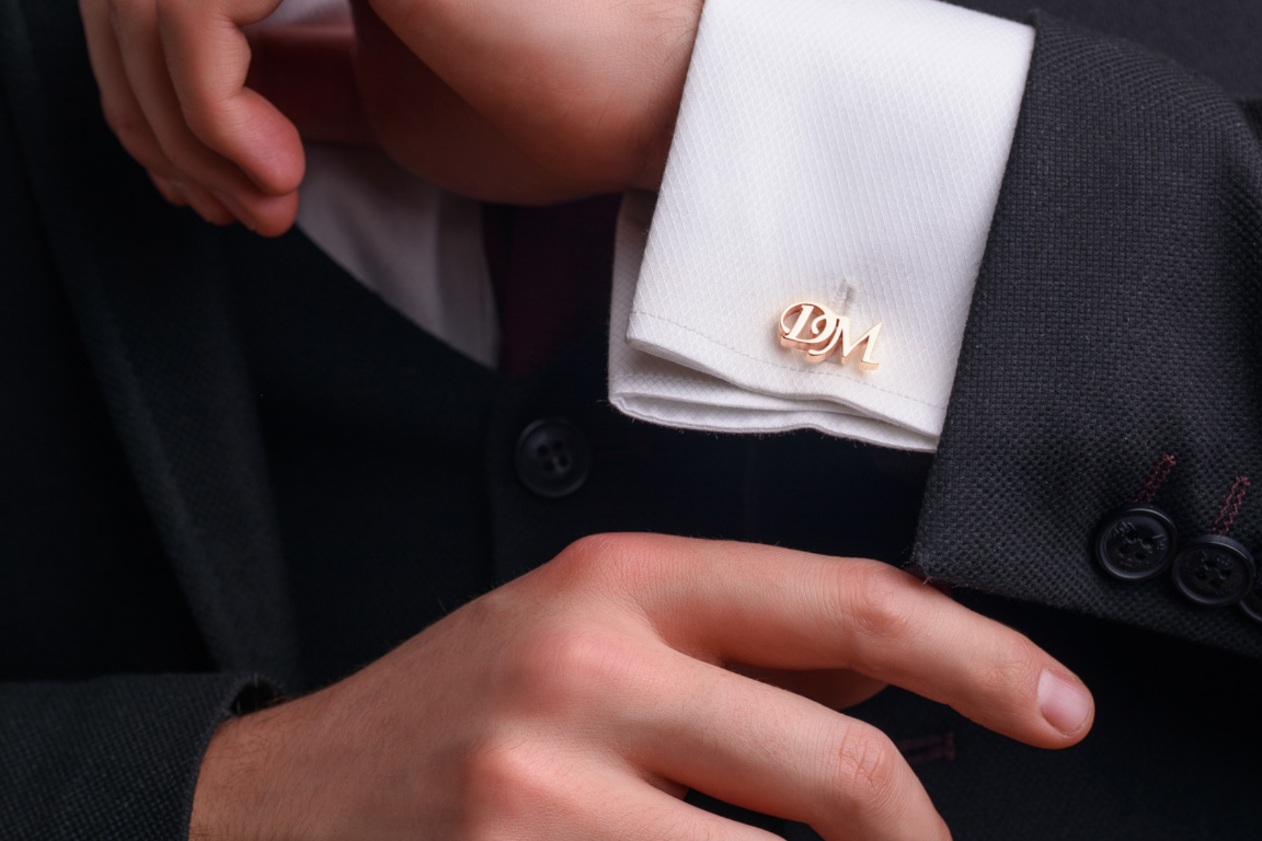 A man in a formal suit with a monogrammed cufflink