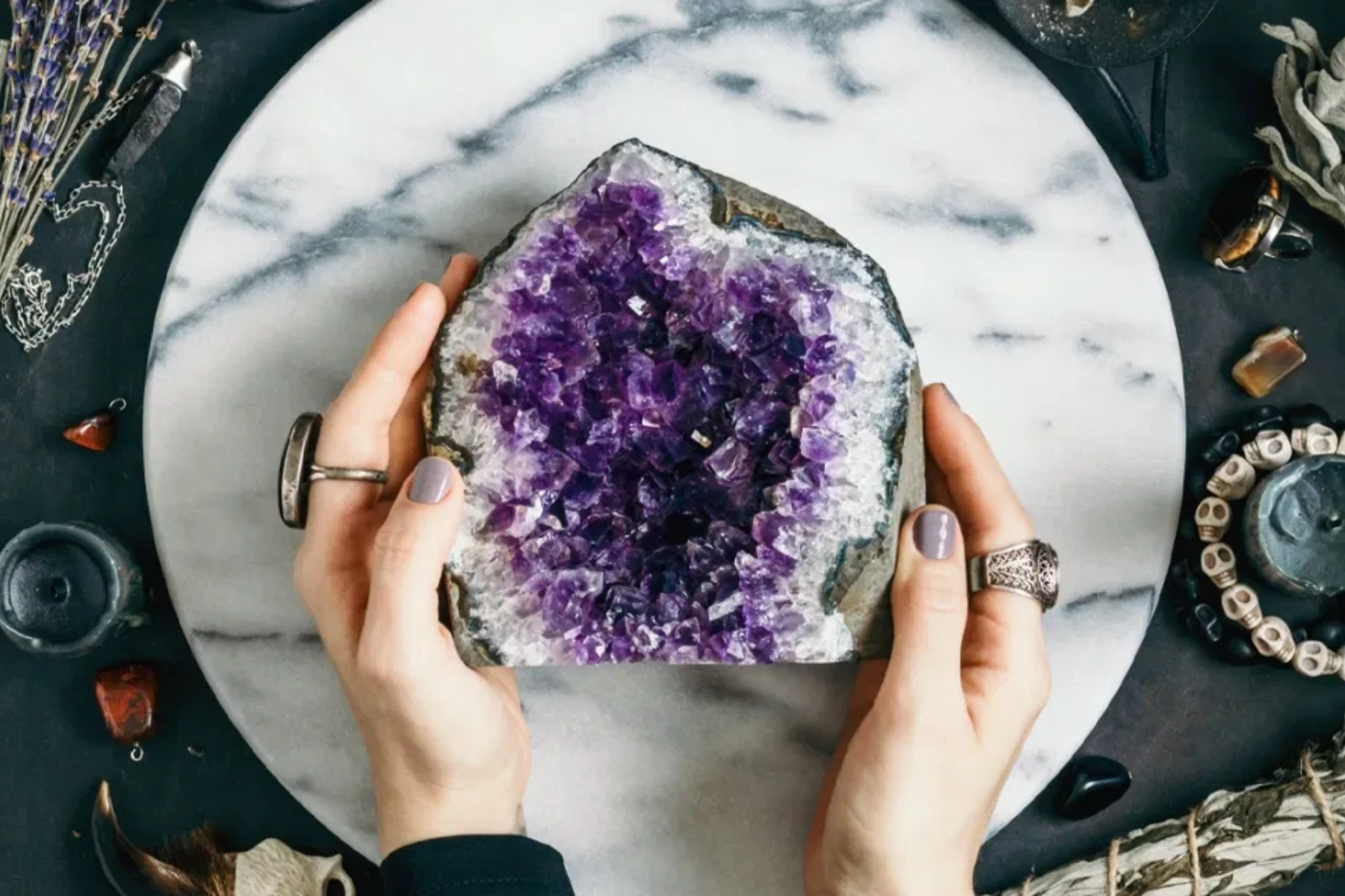 A white-purple amethyst stone is placed on a round white granite by a white hand