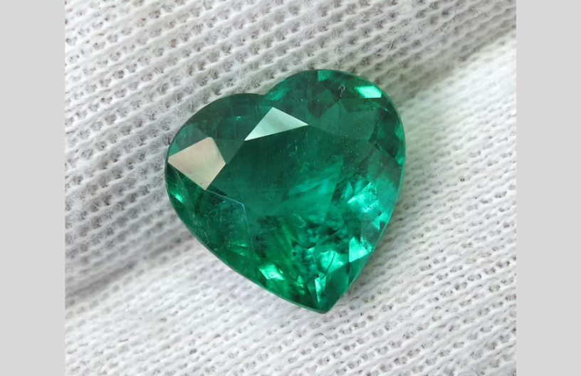 A heart-shaped emerald stone leaning on a cotton