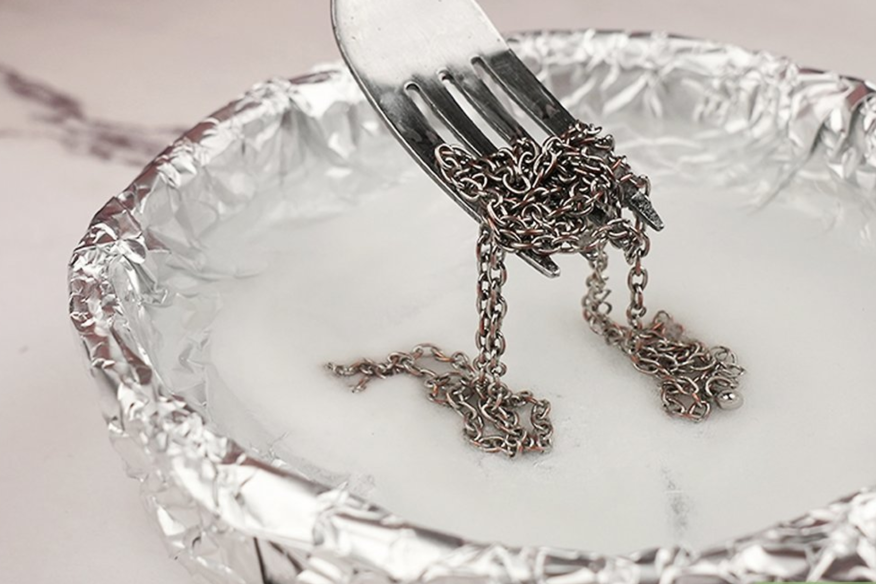 A fork places a silver necklace on a foil containing water