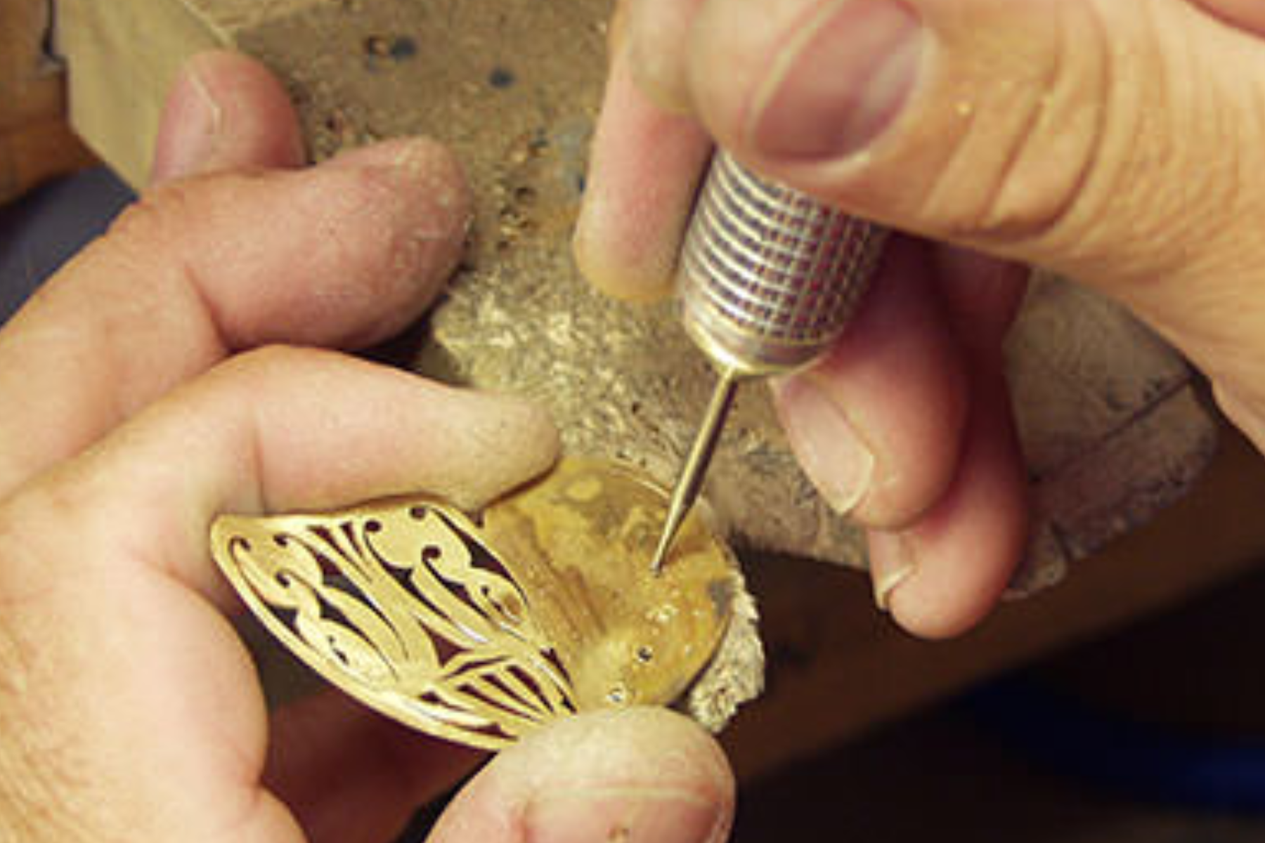 A jeweler's hand engraves a gold piece of jewelry