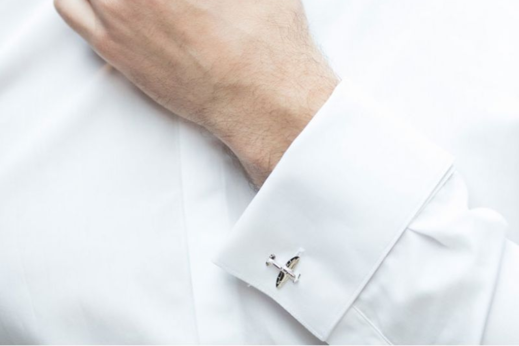 A man wearing a white long sleeve shirt with airplane cufflinks in silver