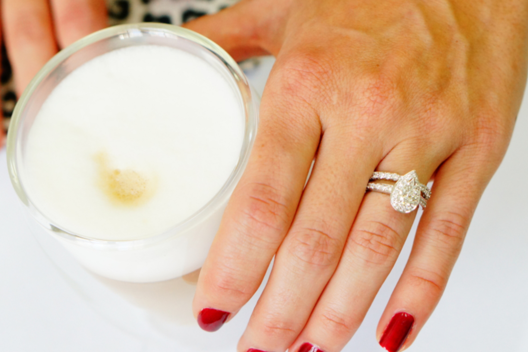 The image depicts a woman's hand with a pear-cut diamond engagement ring being cleaned with a white chemical