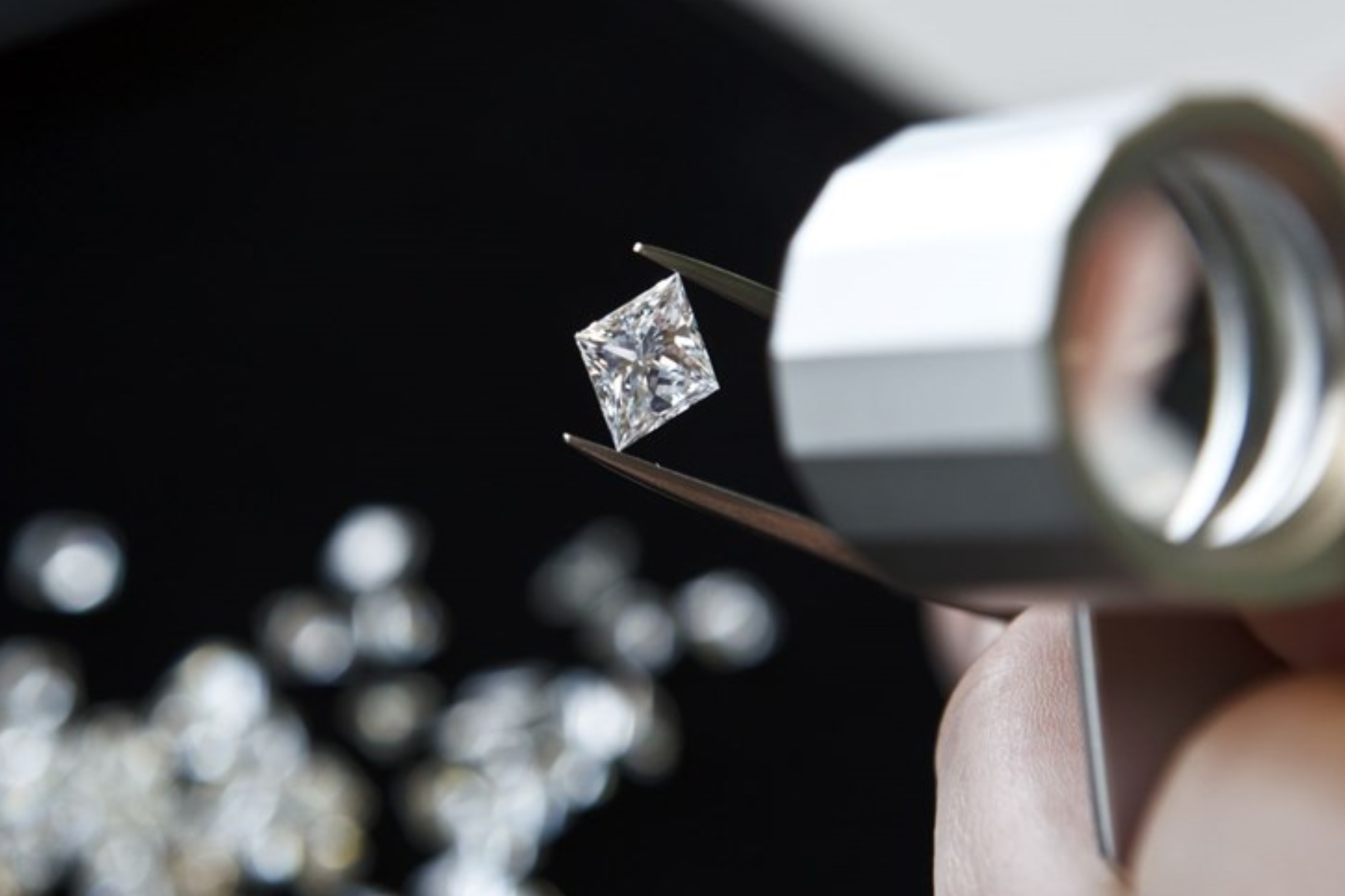 A diamond professional inspects a princess-cut diamond with a lense