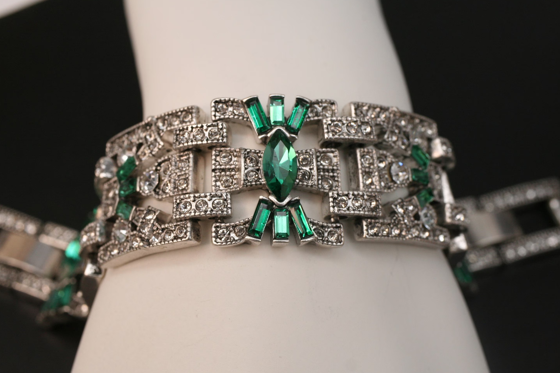 A white woman's hand holding a retro-style bracelet with green stones