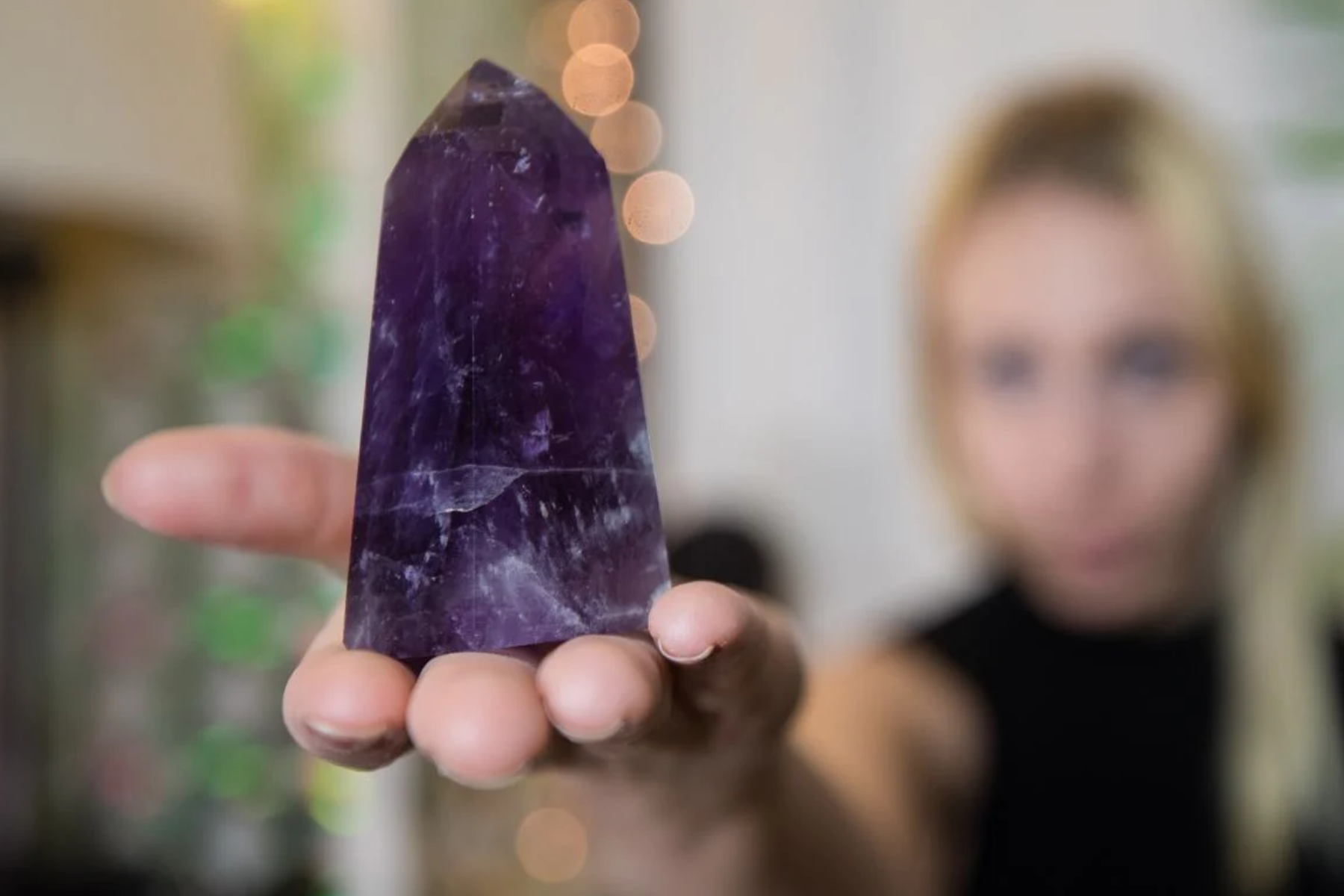A blurred woman in the background holds an amethyst stone that is focusing on a camera