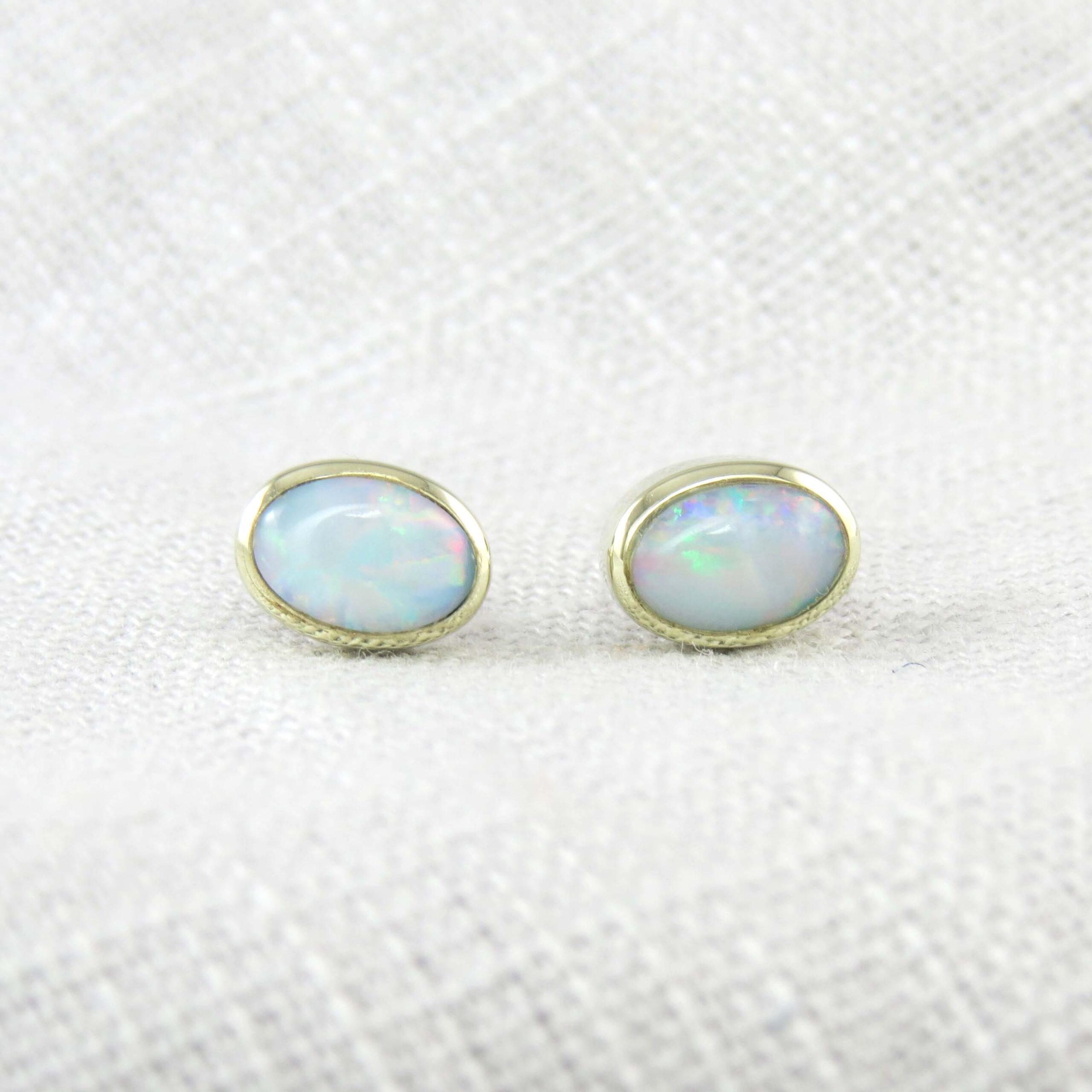 A pair of oval cabochon opals in a pale blue in colour with flashes of pink, green and yellow