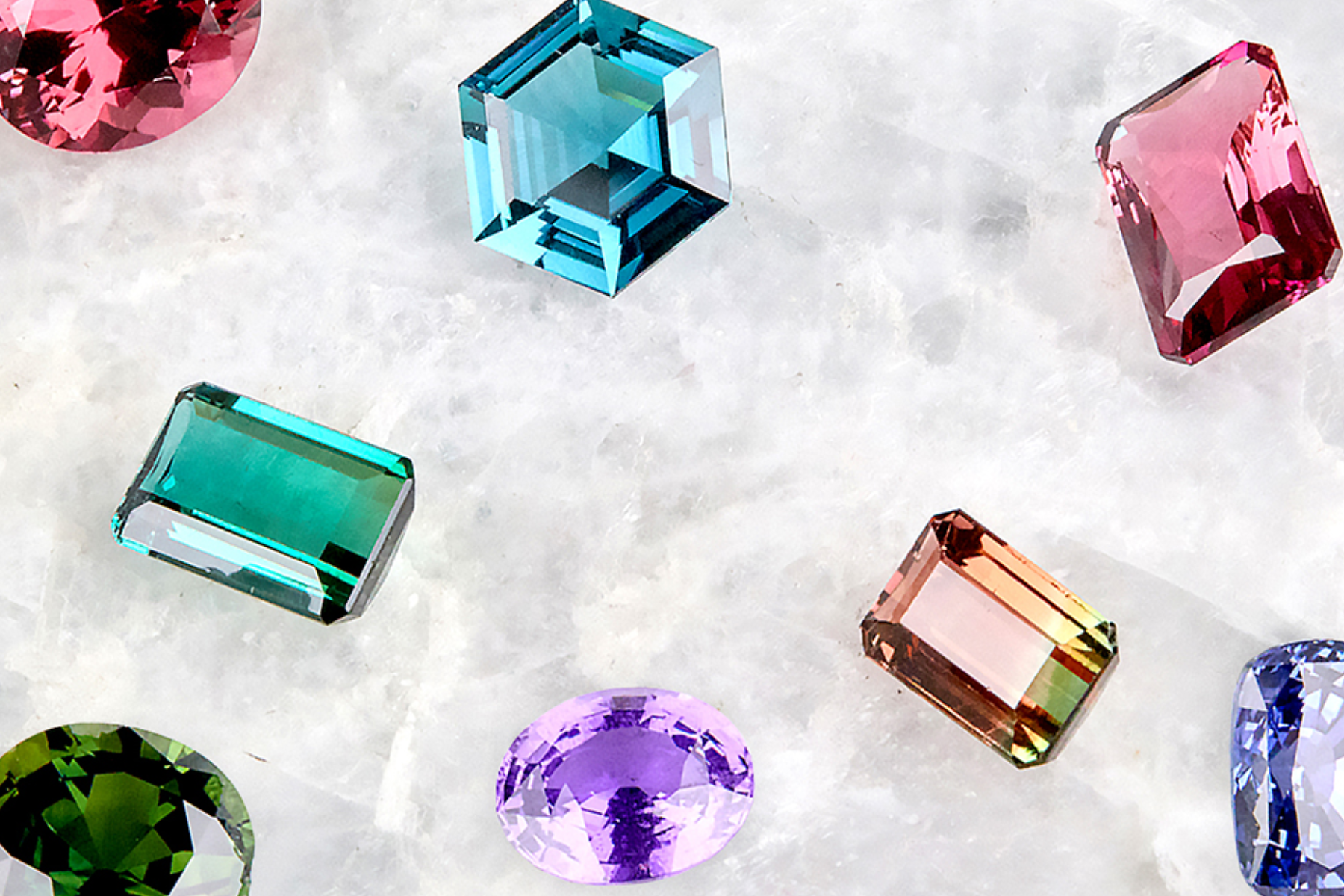 The image depicts eight colored gemstones placed on a white-gray background