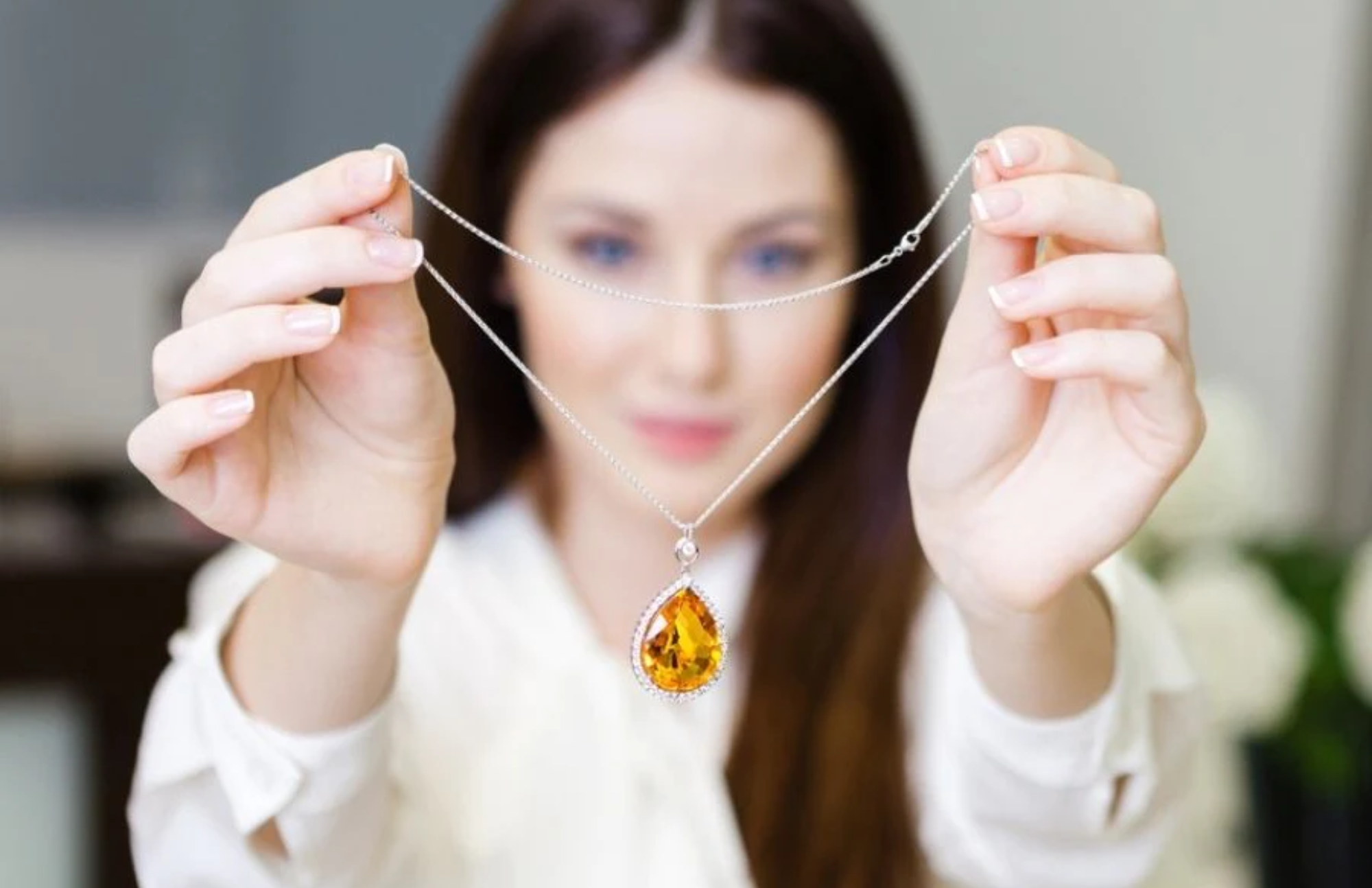 A white woman holds a lace with a yellow topaz pendant