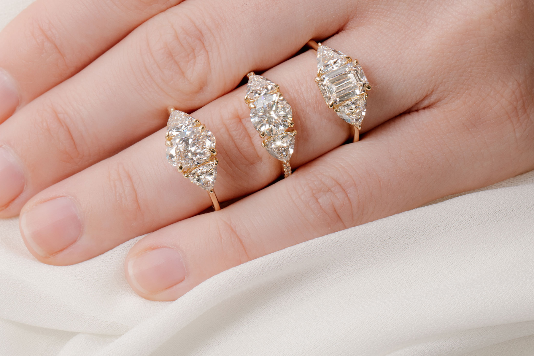 A close-up of a woman's hand showcasing three engagement rings, each with three stones