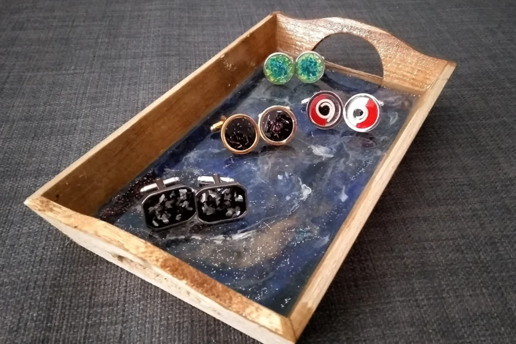 Four space-themed cufflinks on a wooden tray