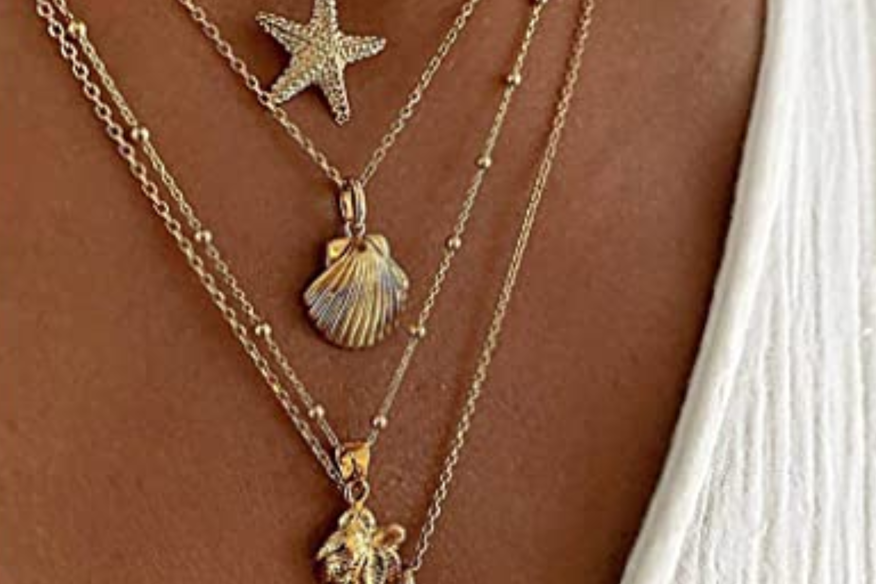 A close-up of a woman's neck and chest area, showing her wearing multiple shell pendant necklaces layered on top of each other
