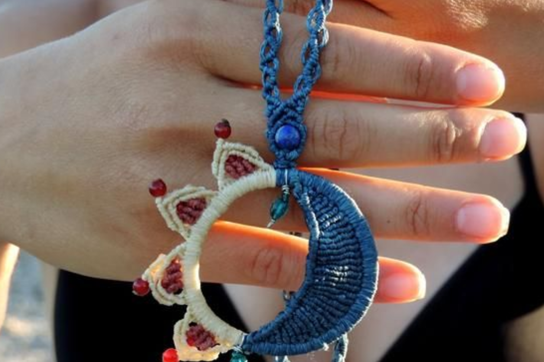 A woman's hand holding a handcrafted sun and moon necklace