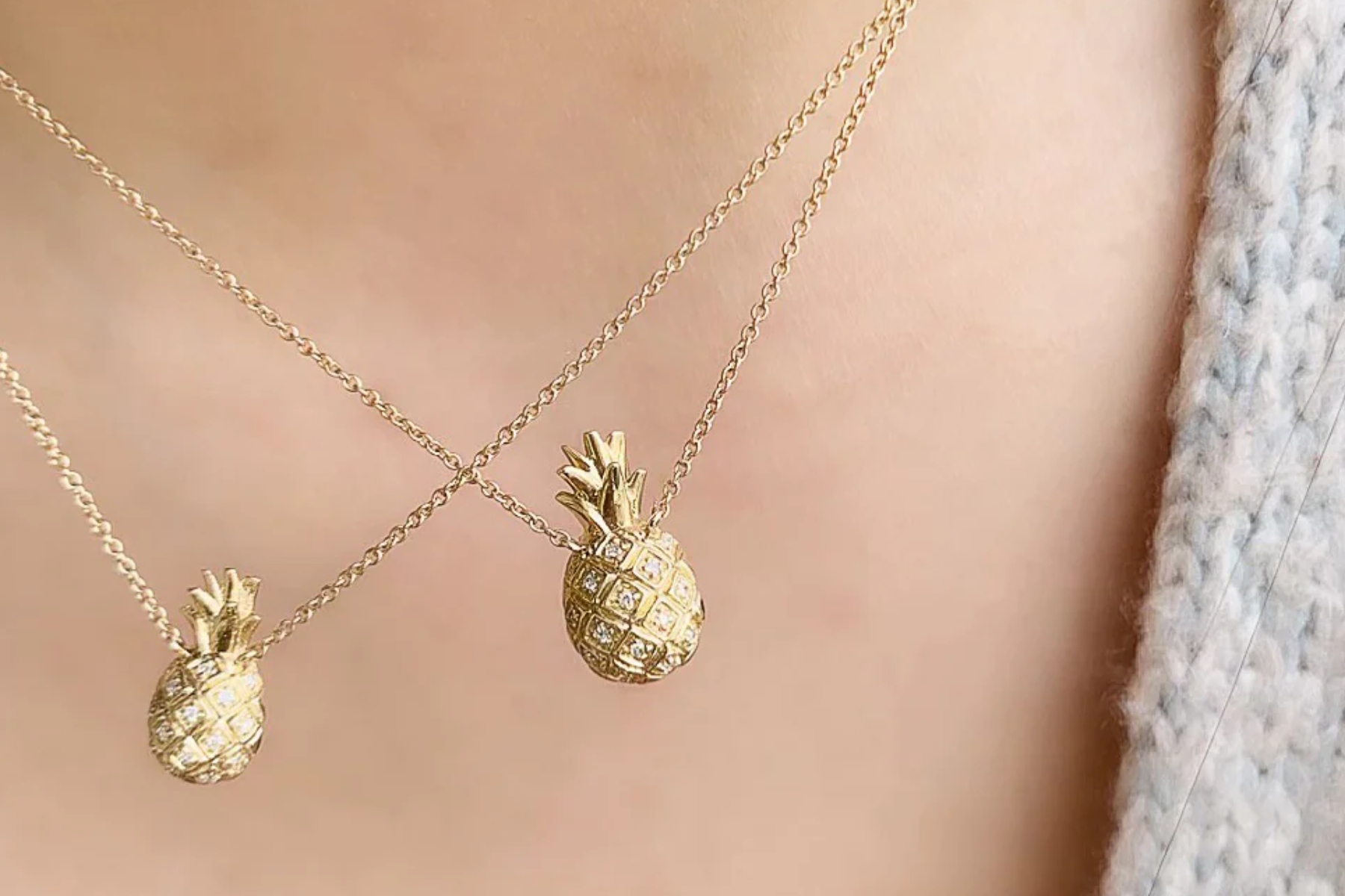 Two gold pineapple necklaces on a woman's neck