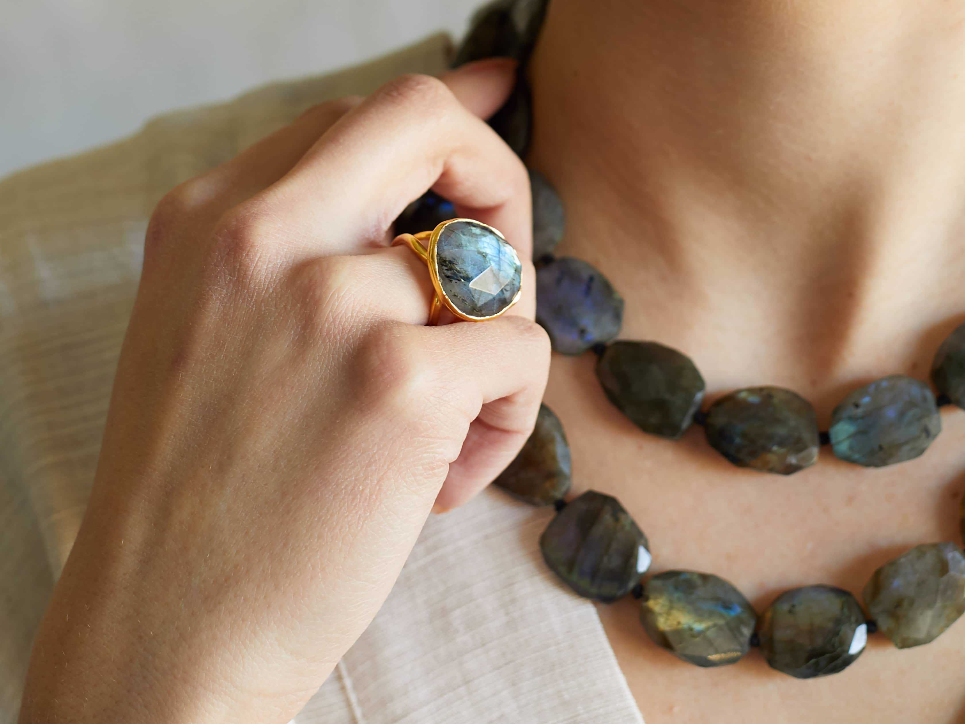 A labradorite ring on a woman's hand, along with multiple stone necklaces around her neck