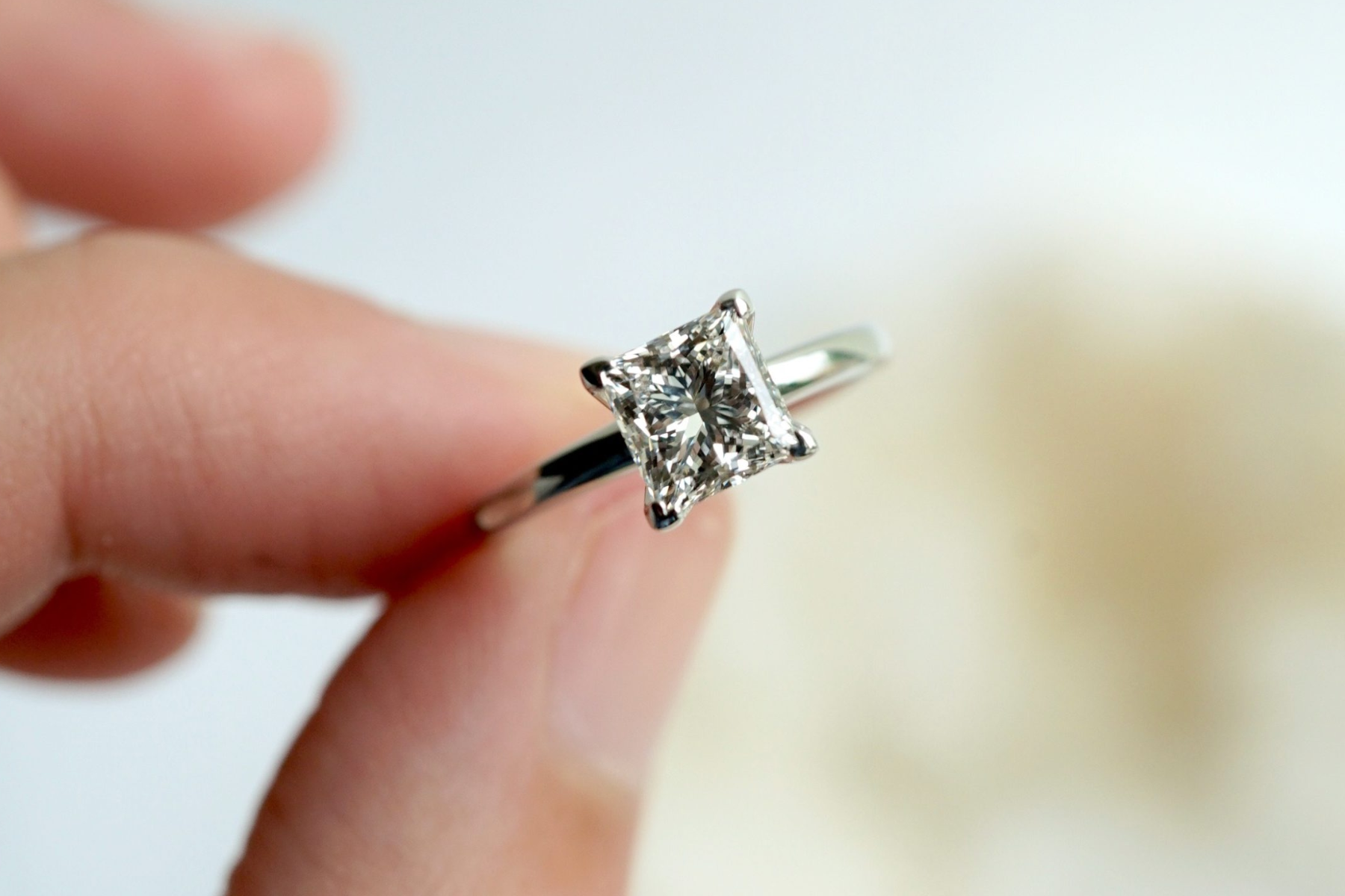 A hand wearing a diamond ring with a princess-cut stone held by a woman