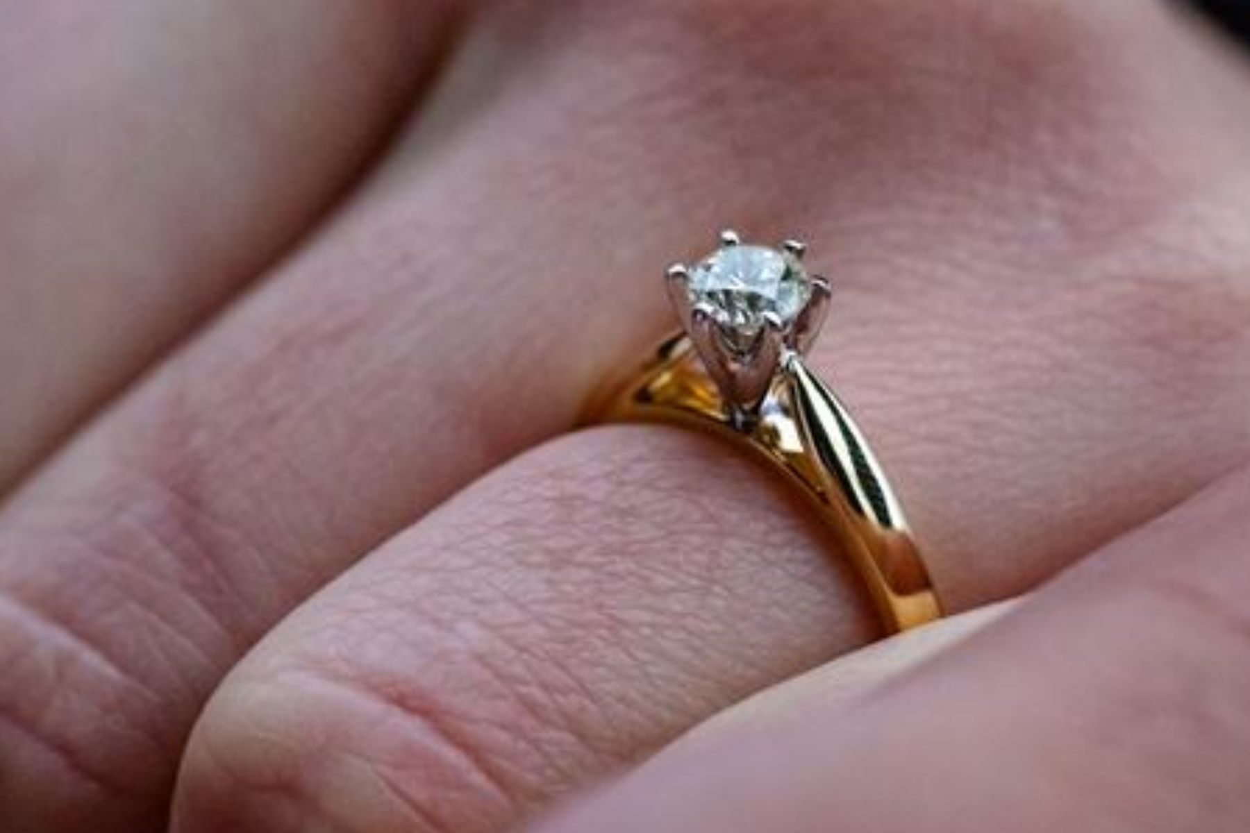 A gold band engagement ring with a diamond stone on a finger