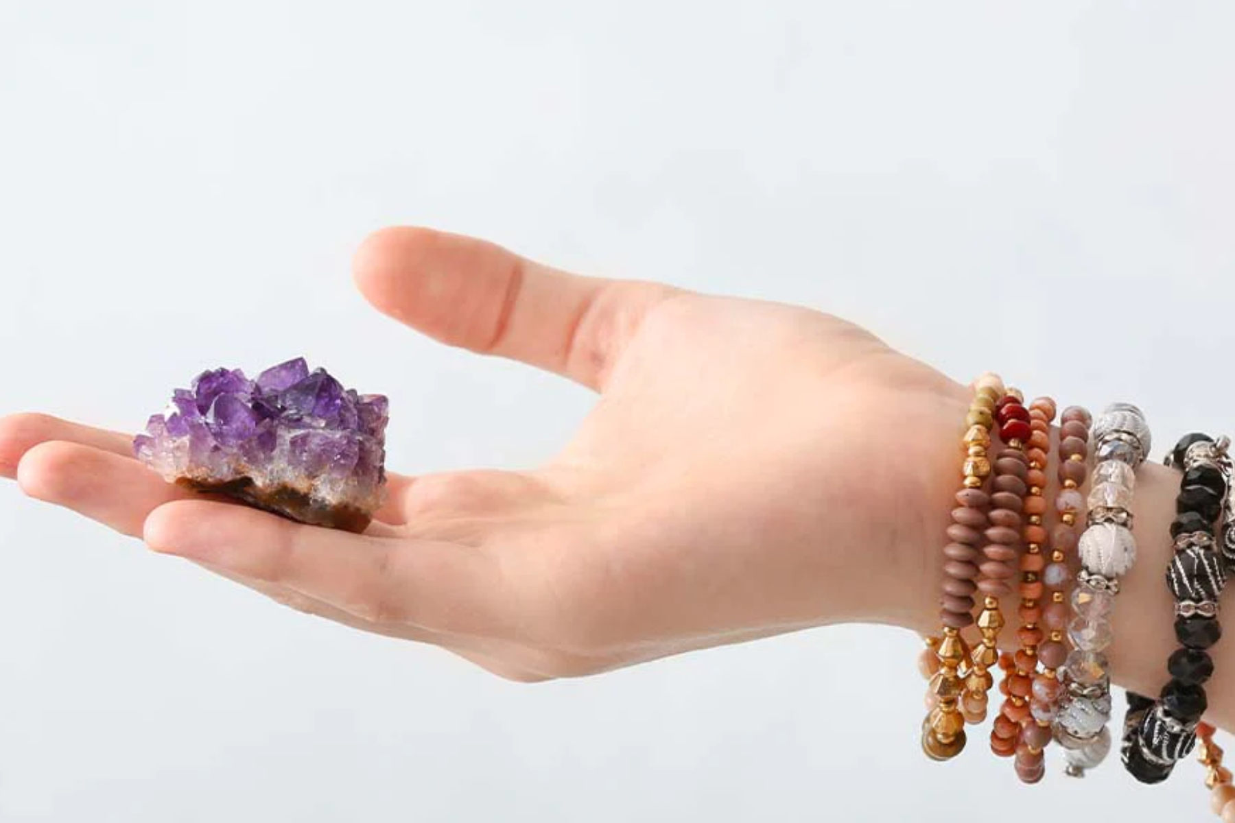 A close-up of a woman's hand showcasing a small raw amethyst resting on her palm