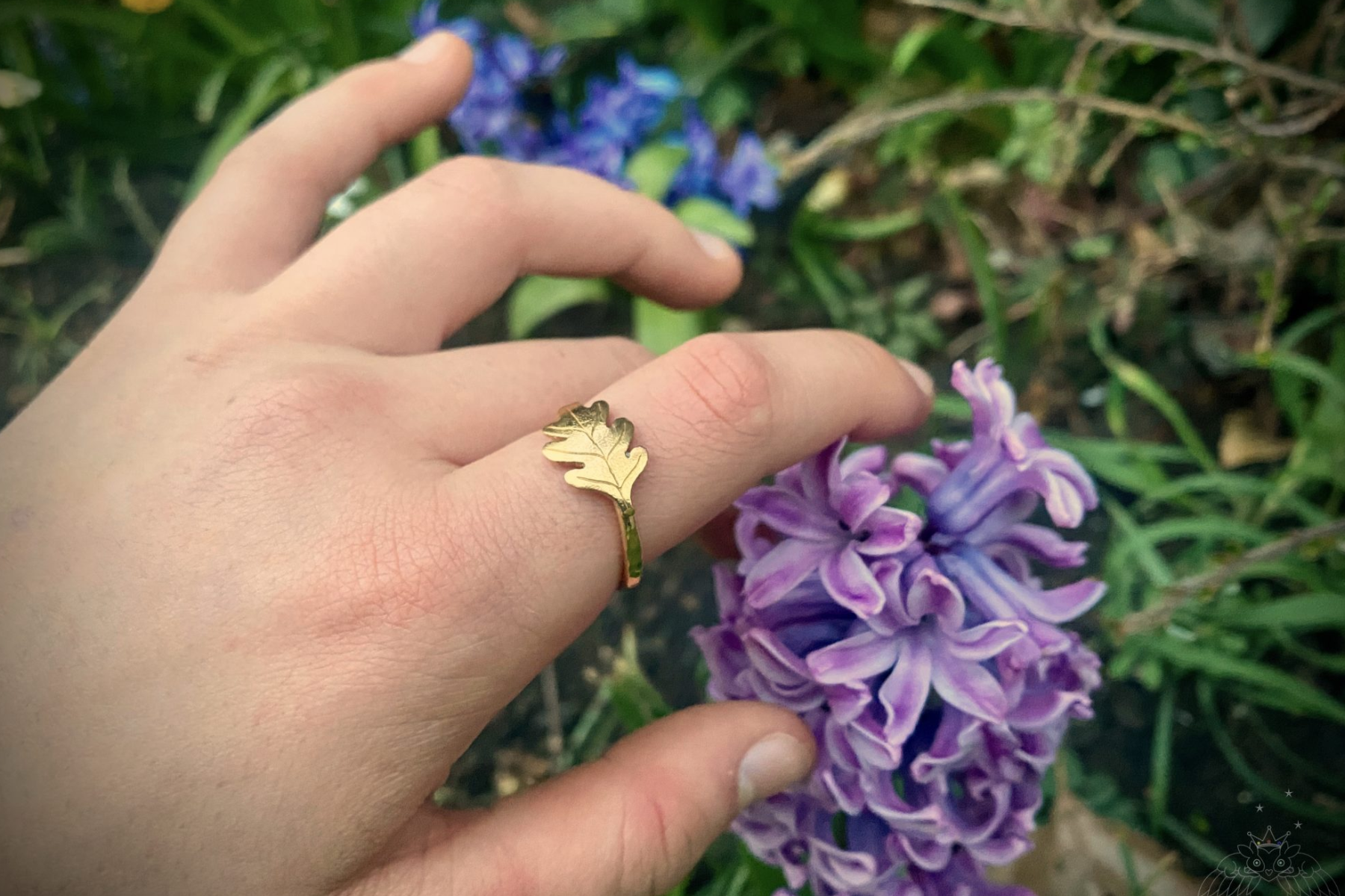 Gold leaf ring on a woman's finger holding a purple flower