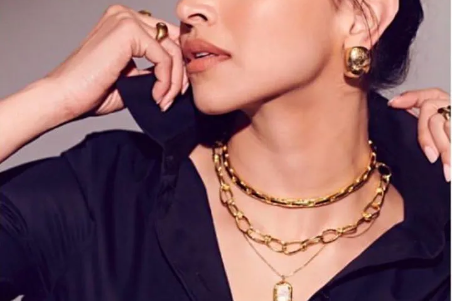 A woman in a dark blue gown wearing a gold layered-chain necklace with gold rings and earrings