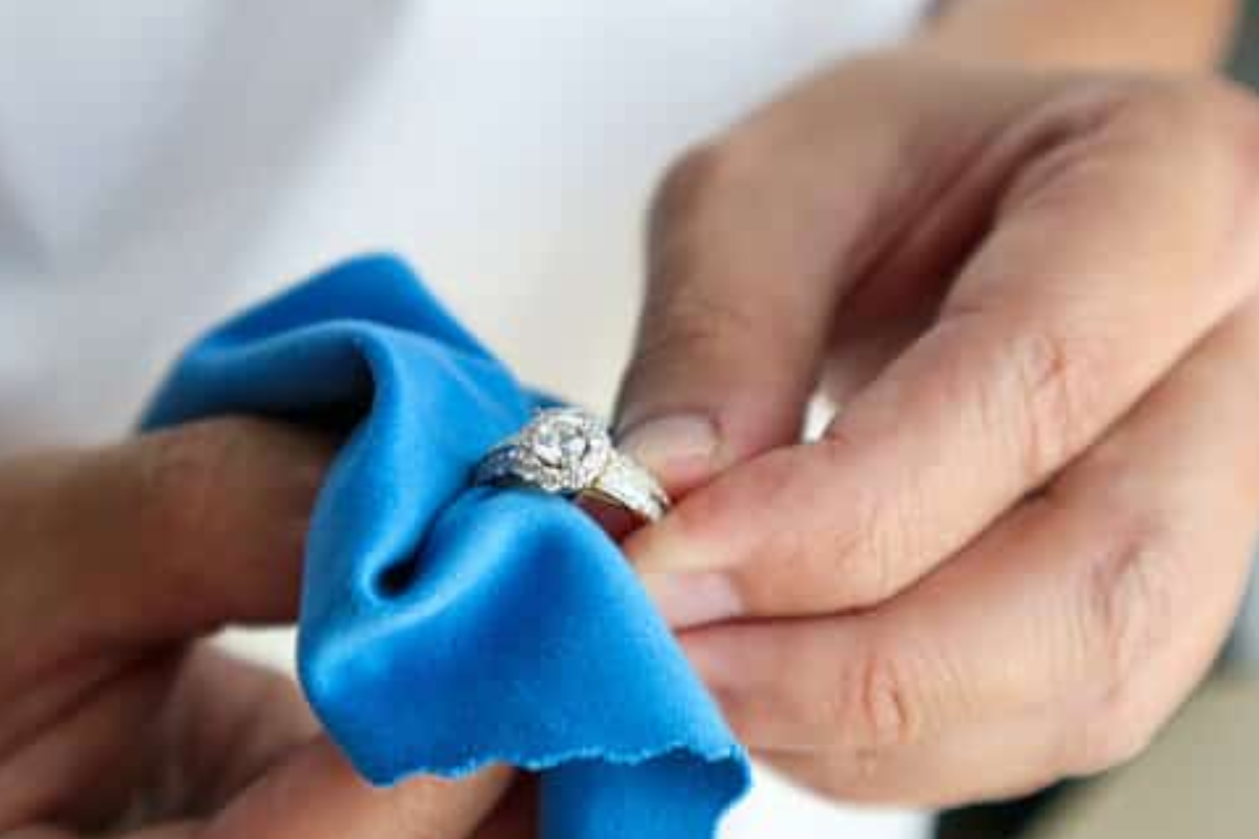 Blue cotton is used by an individual's hand to clean a ring