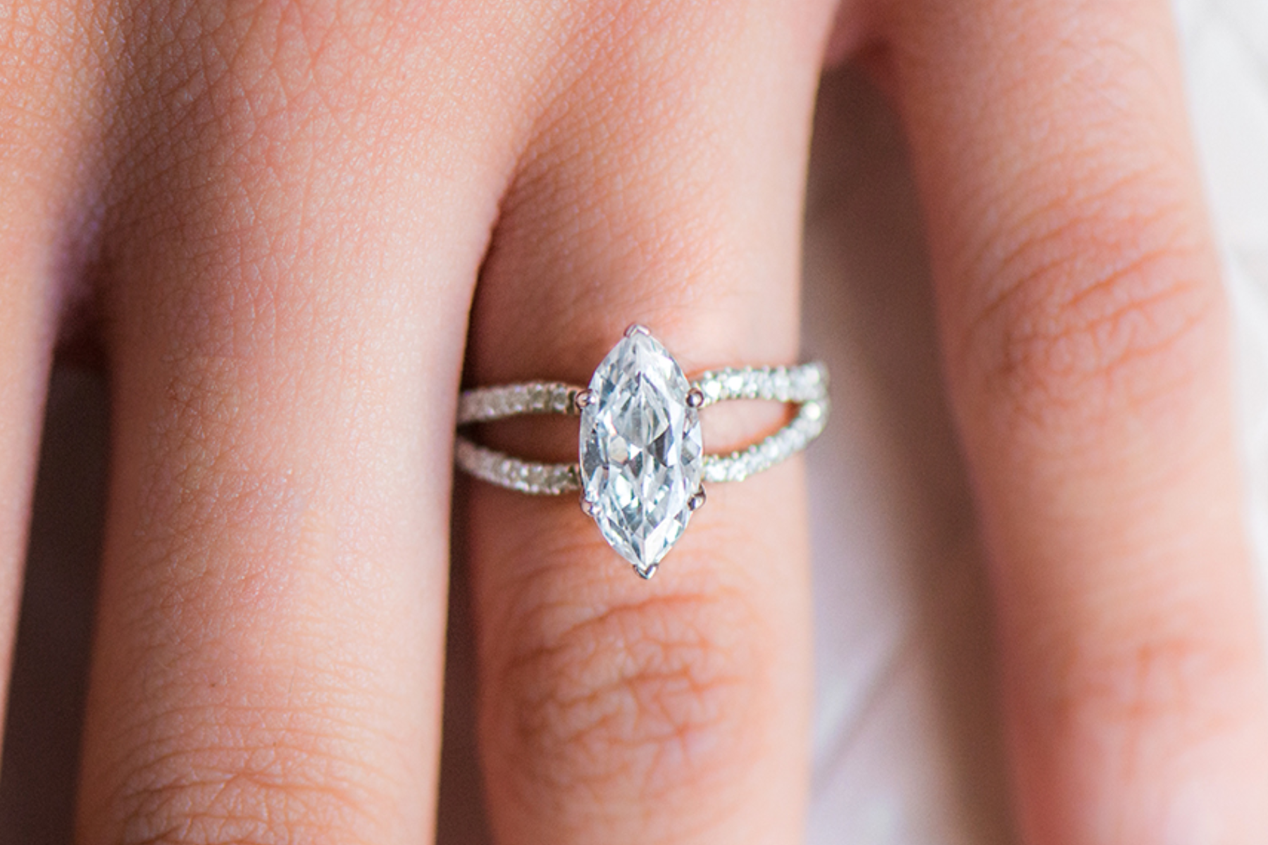 A close-up photograph of a woman's hand with a marquise-cut diamond engagement ring on her ring finger