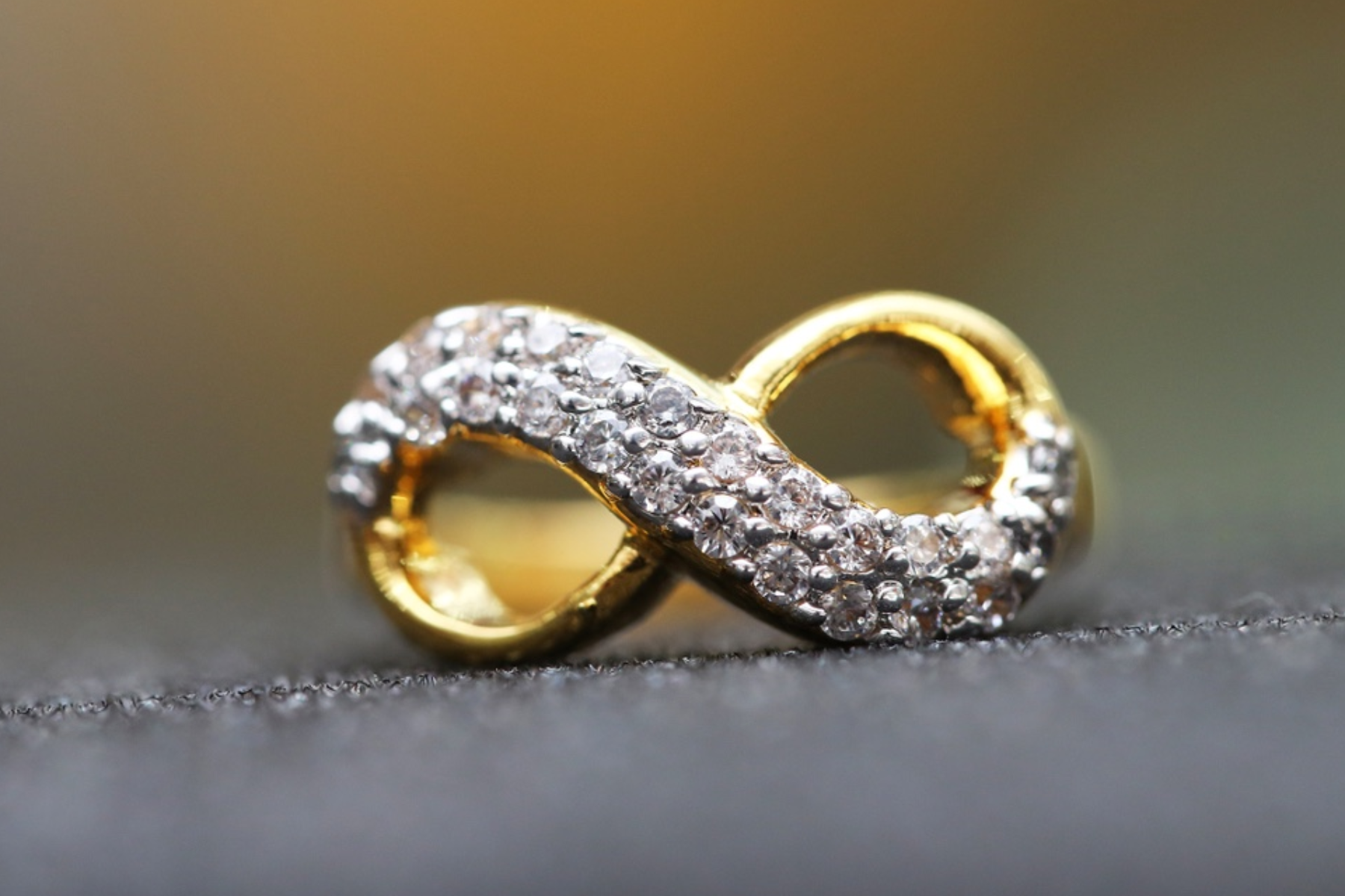 An infinity ring made of gold and diamond, placed on a background with a blurred effec