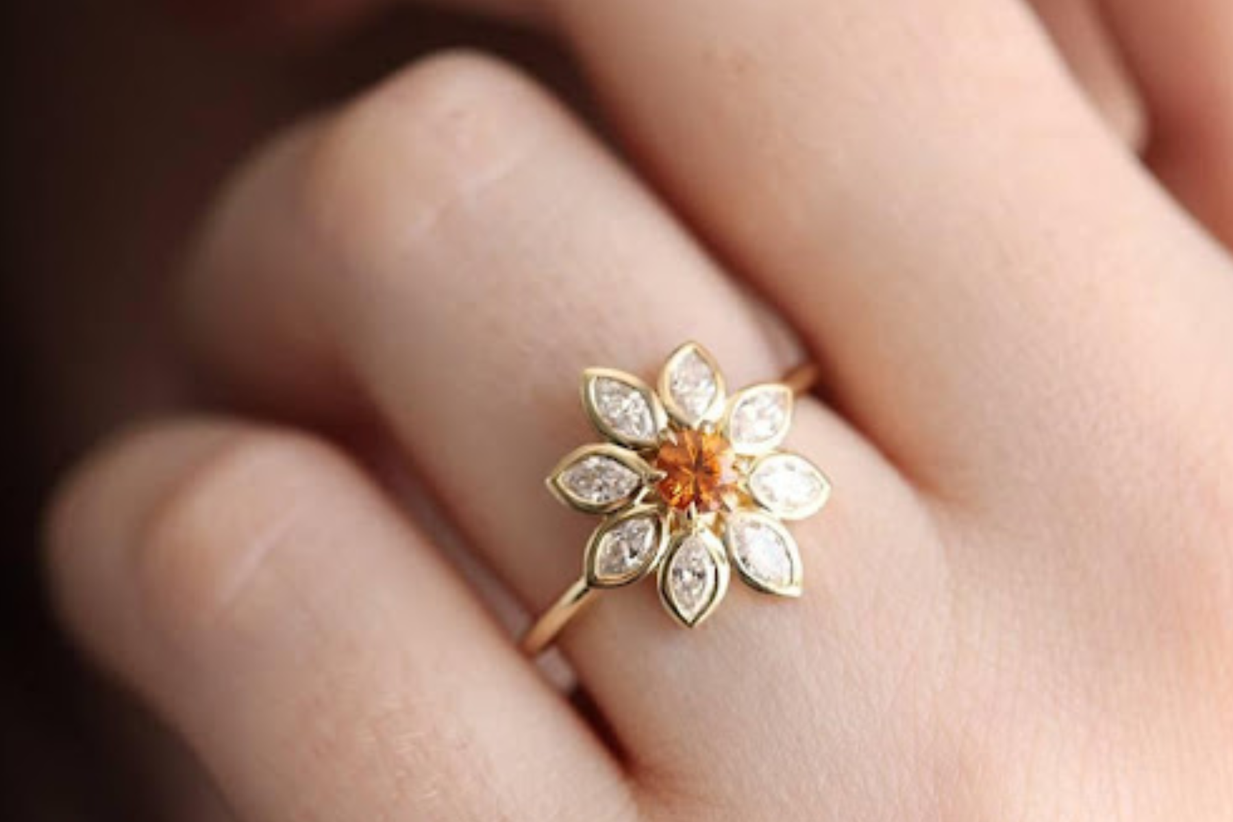 A close-up image of a woman's finger adorned with a ring featuring a floral design inspired by nature