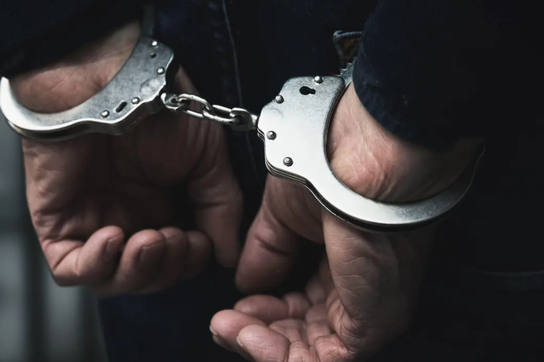 A close-up photograph of a man's hands, which are handcuffed together