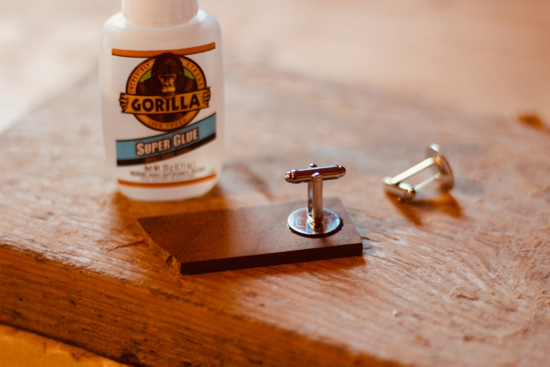 Wooden cufflinks and a container of super glue placed on a wooden surface