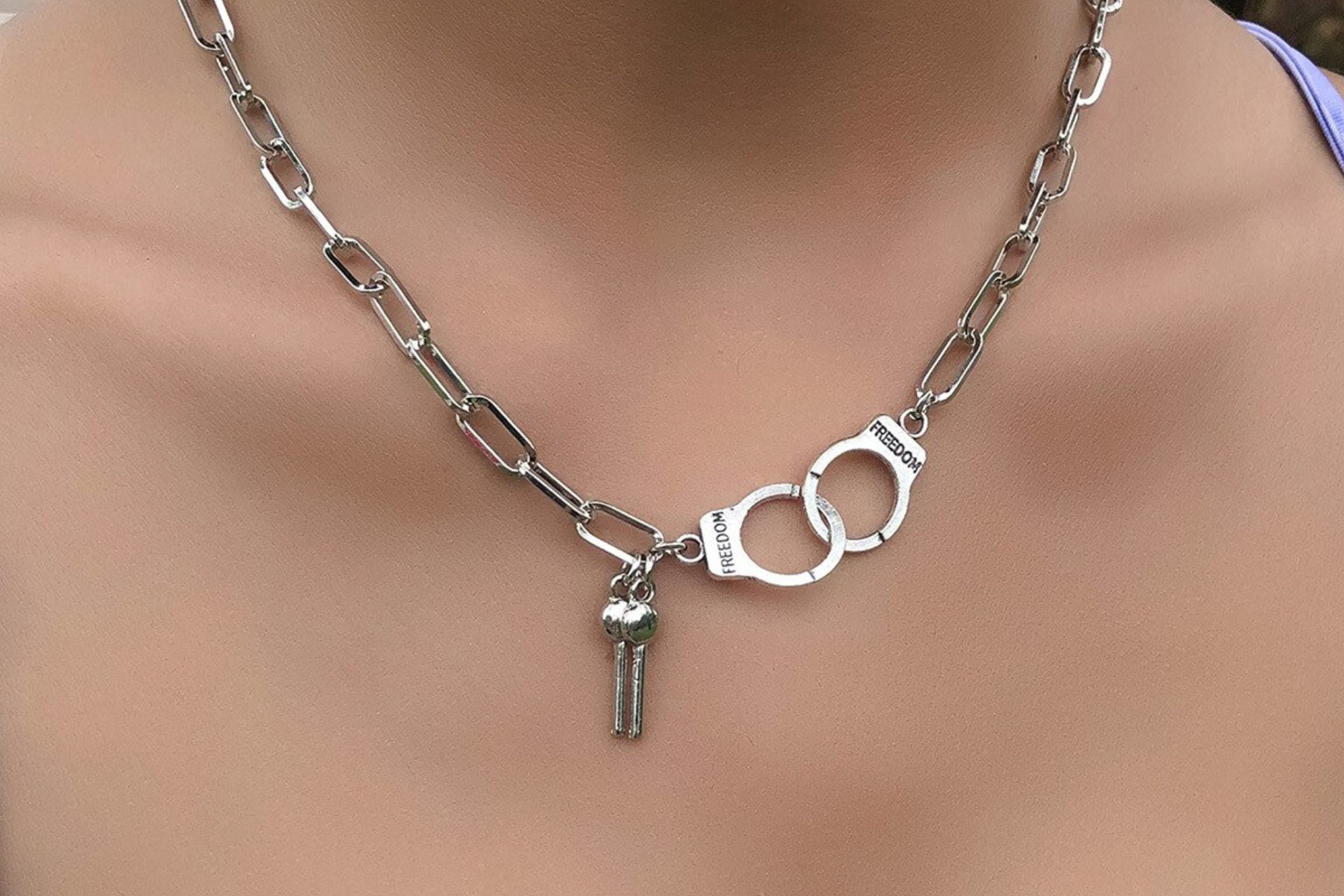 A photograph of a necklace featuring a lock and key handcuff design, worn around a woman's neck in a close-up view