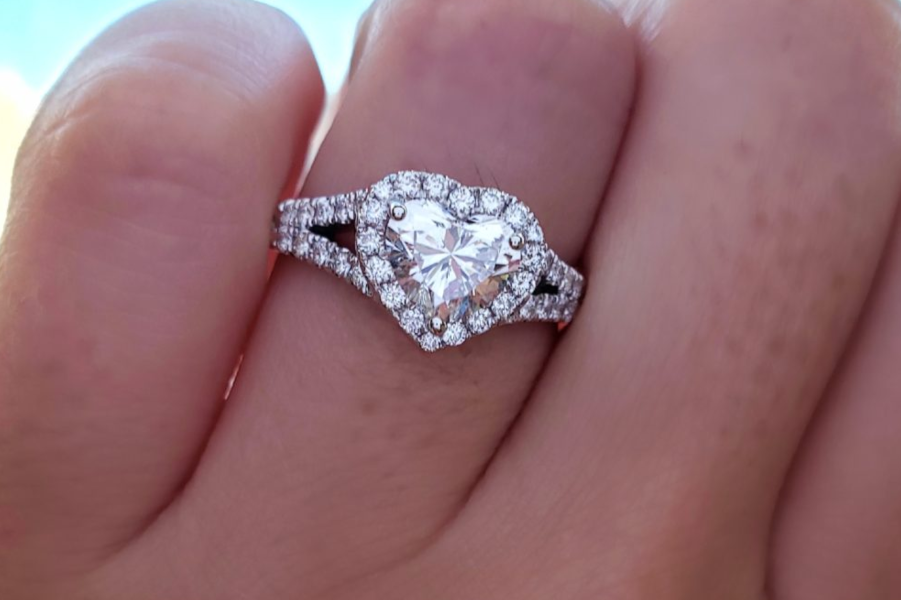 A heart-shaped diamond engagement ring on a woman's ring finger in close-up view
