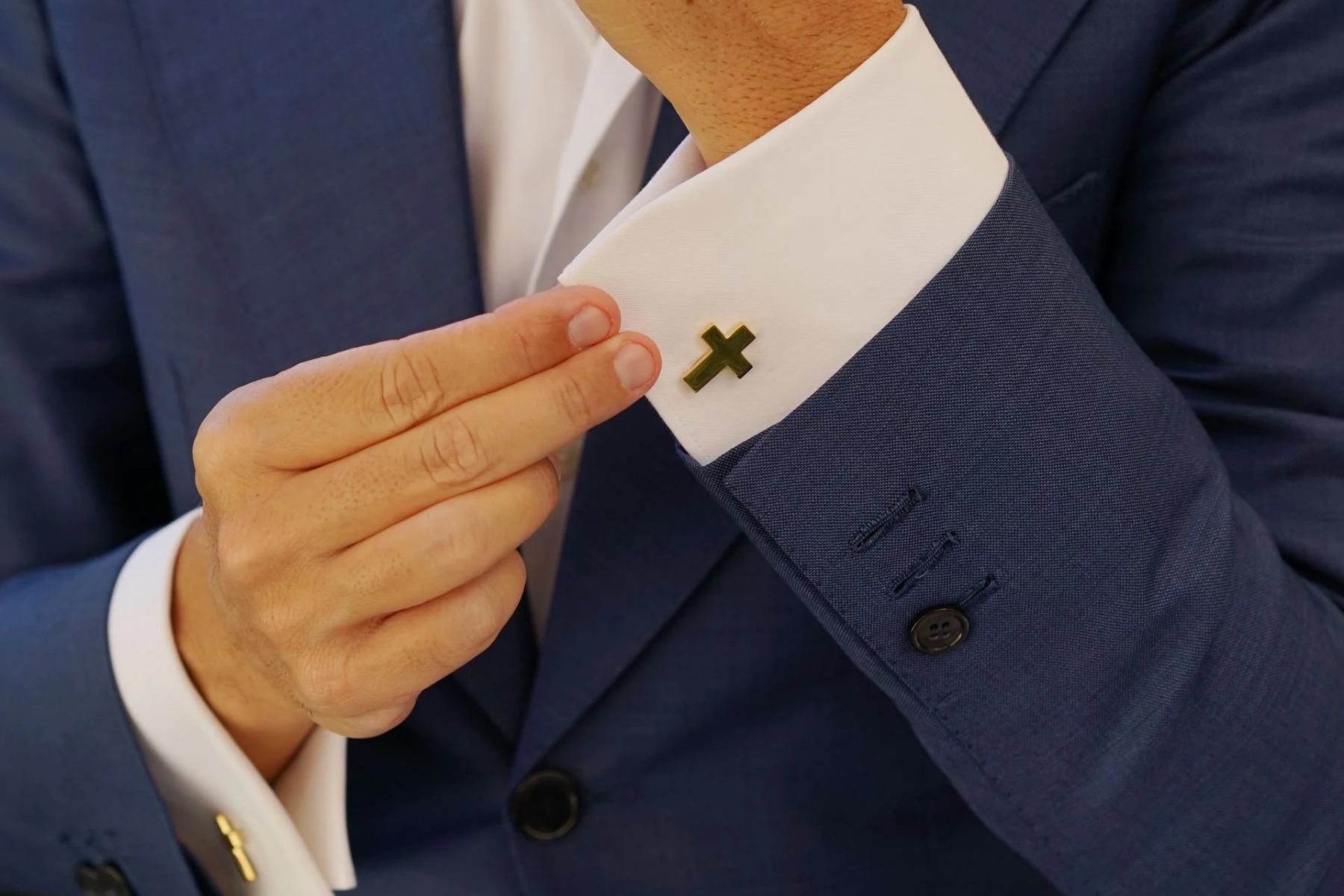 A navy blue suit with gold cross cufflinks worn by a man