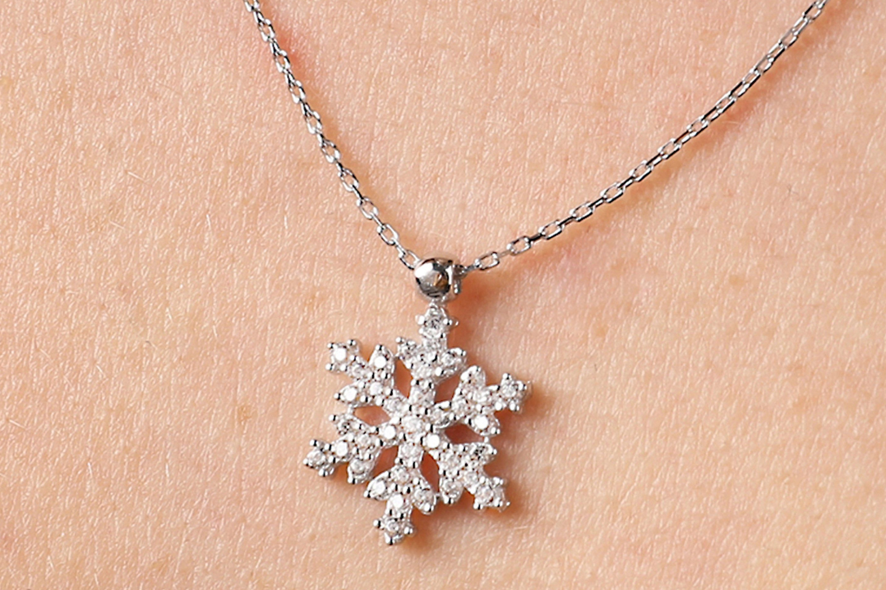 A close-up photograph of a snowflake necklace resting on a person's skin