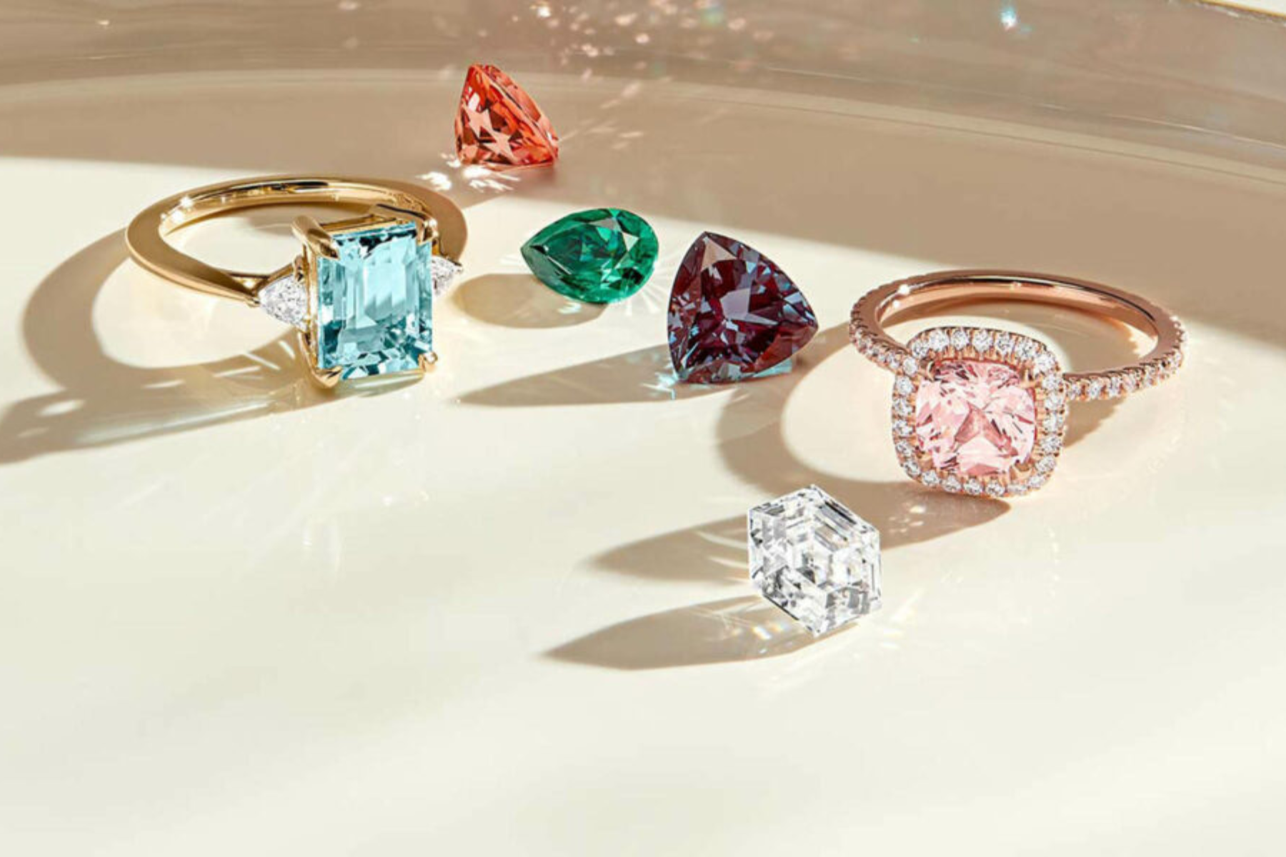 A photograph of two engagement rings, one with a blue gemstone and the other with a pink gemstone, both surrounded by four additional colored gemstones