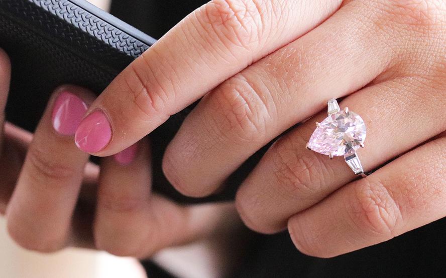 A woman's hand holding a mobile phone with a pink diamond ring on her finger