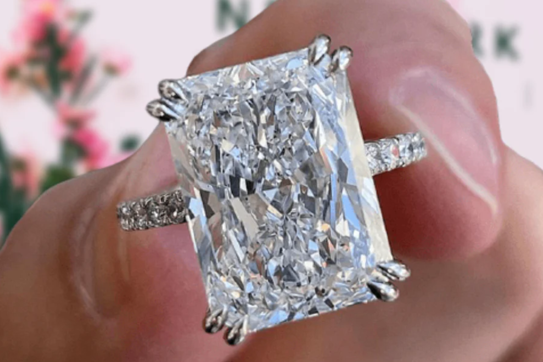 A close-up photograph of a hand carrying an engagement ring with a large radiant-cut diamond