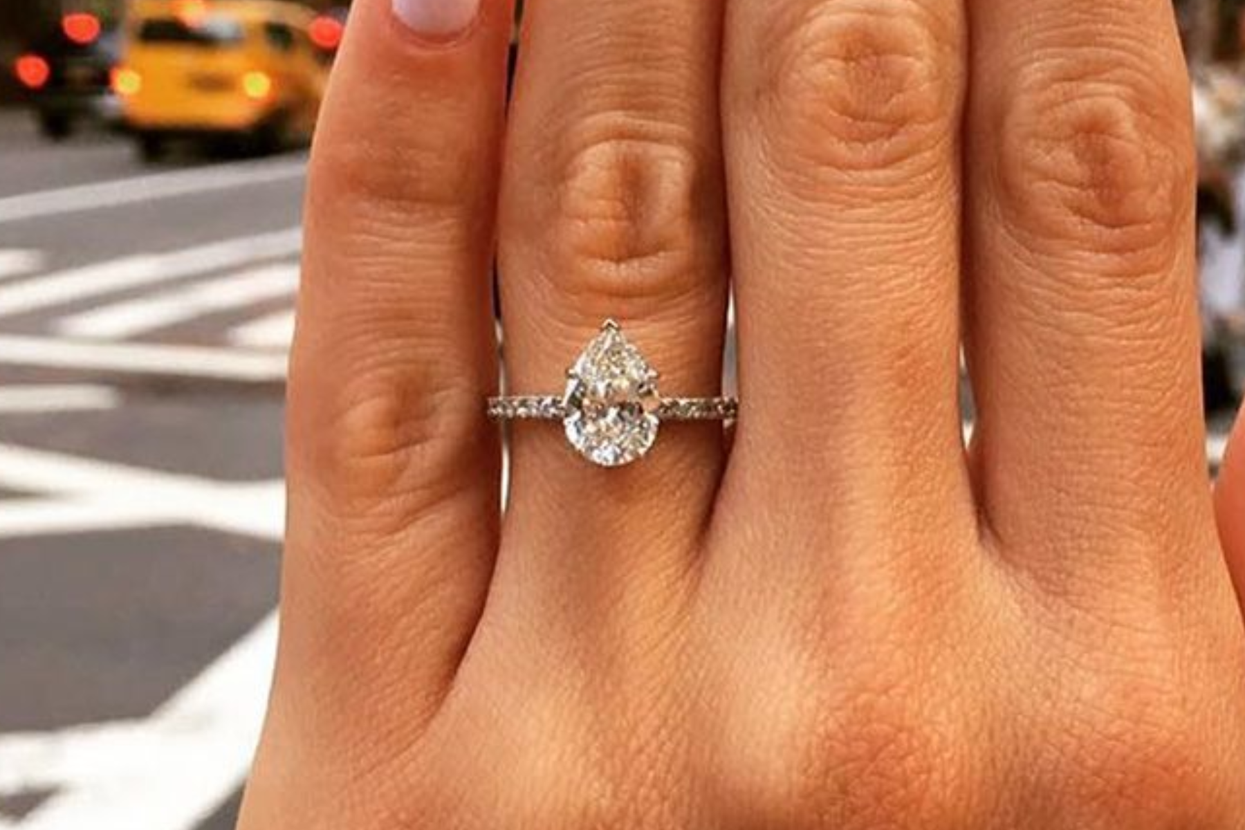 A woman's hand wearing a pear-cut diamond engagement ring in a public setting
