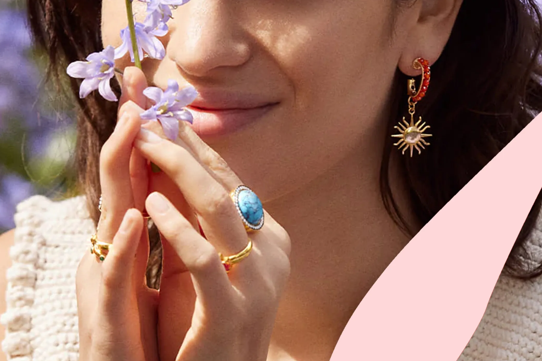 A woman wearing birthstone jewelry as she smells a flower