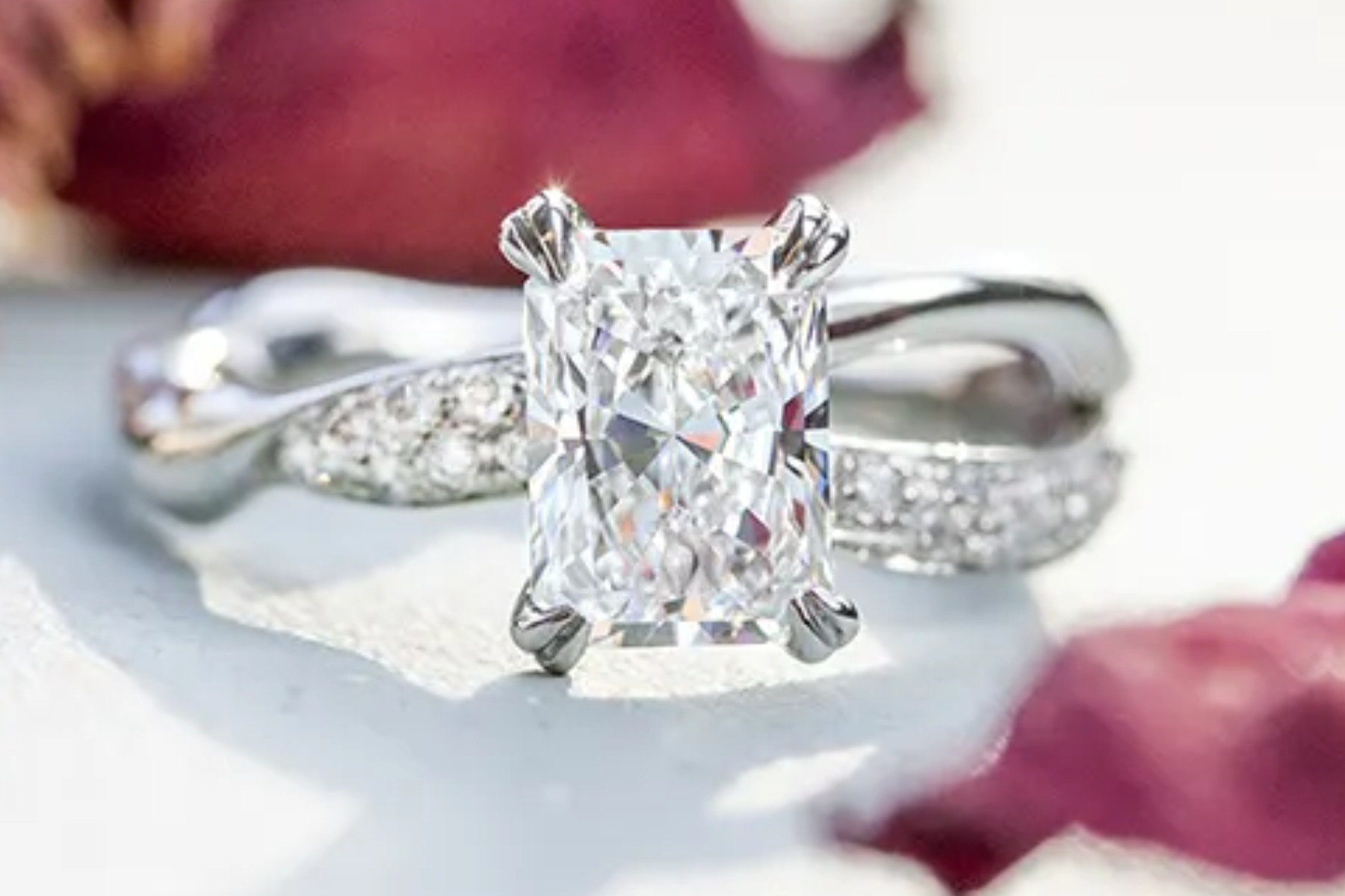 An engagement ring featuring a radiant-cut diamond placed on top of scattered flower petals