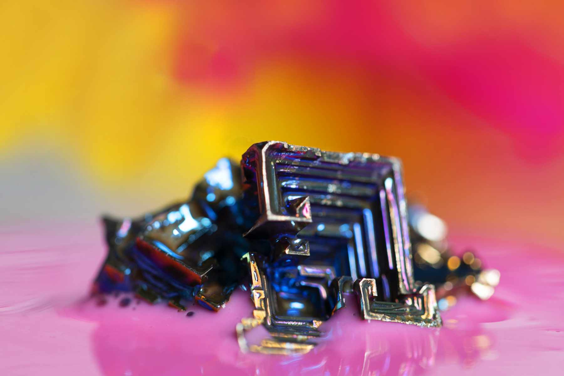 A photograph of a Bismuth crystal placed on a vibrant and colorful background