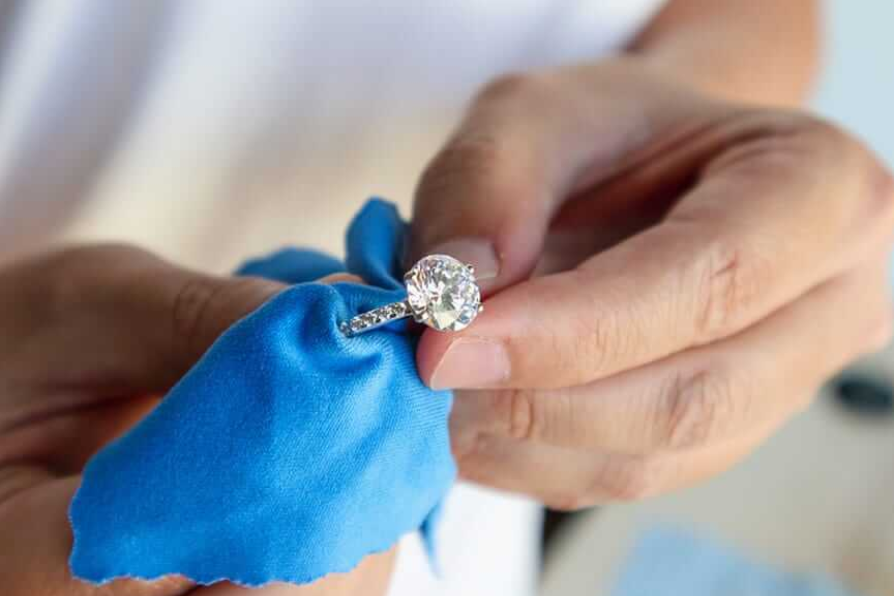 A pave engagement ring being cleaned by a man's hand using blue cotton
