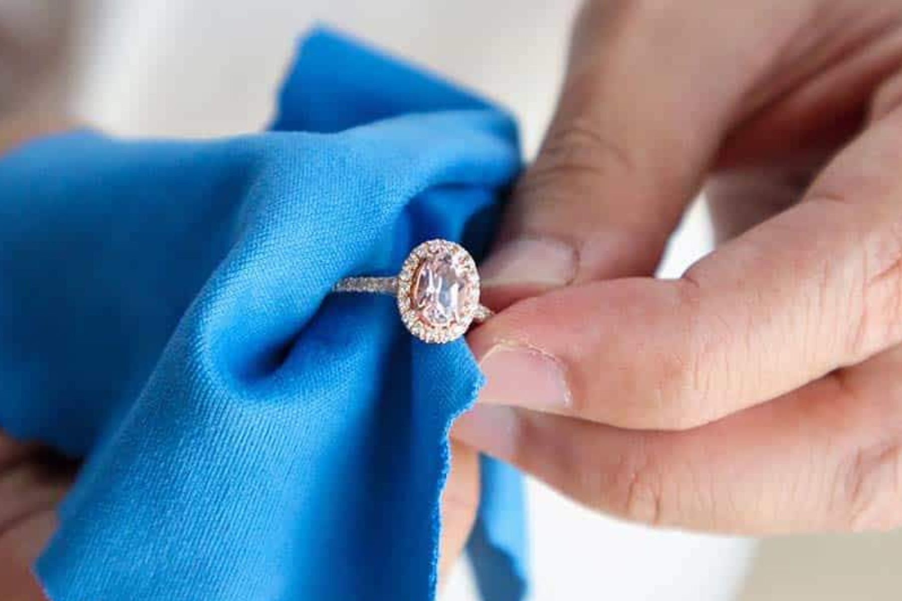 A woman's hand holding a blue cotton cloth while cleaning a colored diamond engagement ring